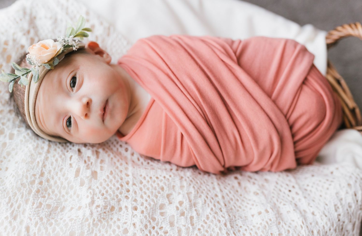 Baby in coral outfit lying on white textured blanket with sweet expression.