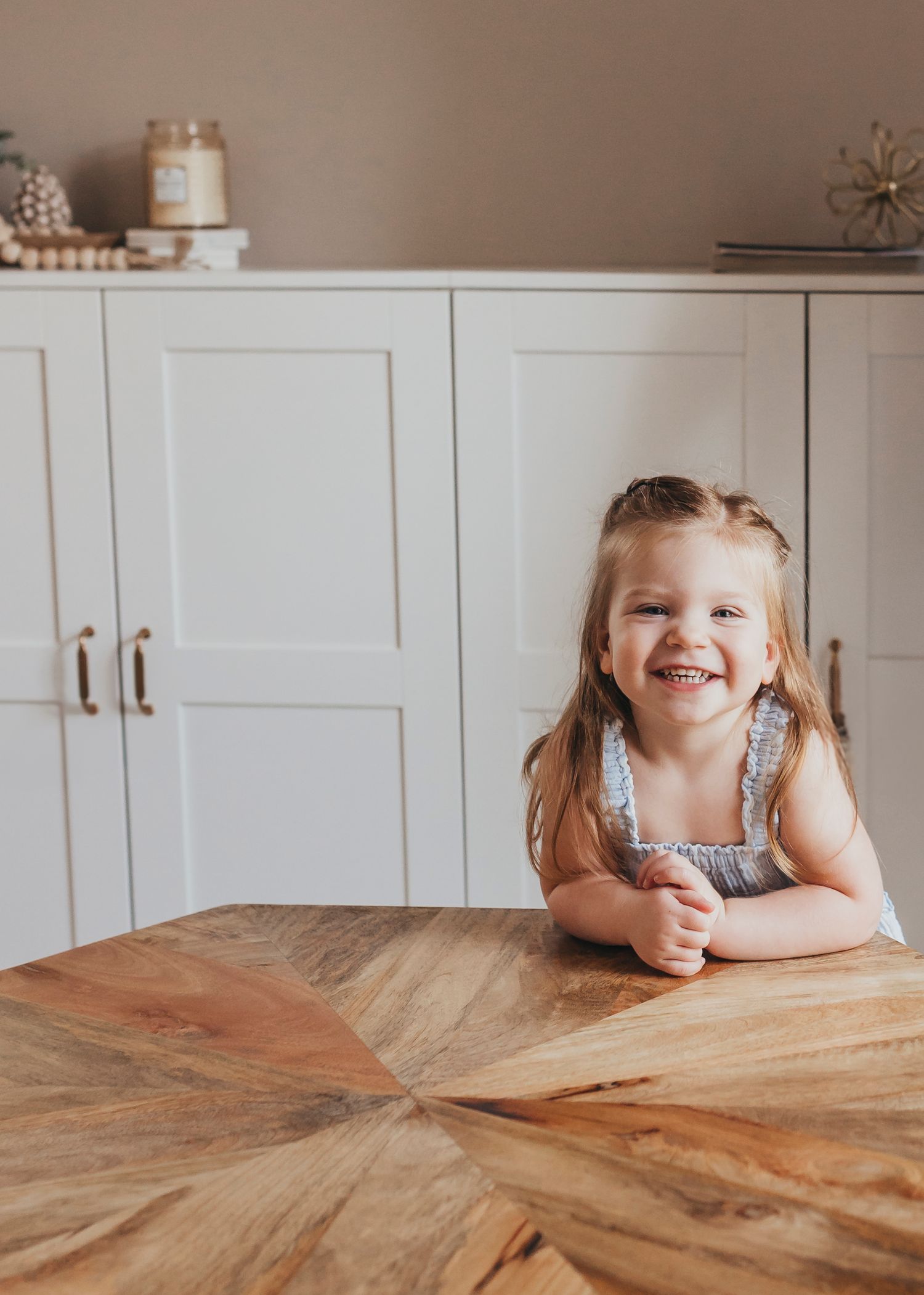 Young child peeks over wooden table edge with a bright smile during candid moment.