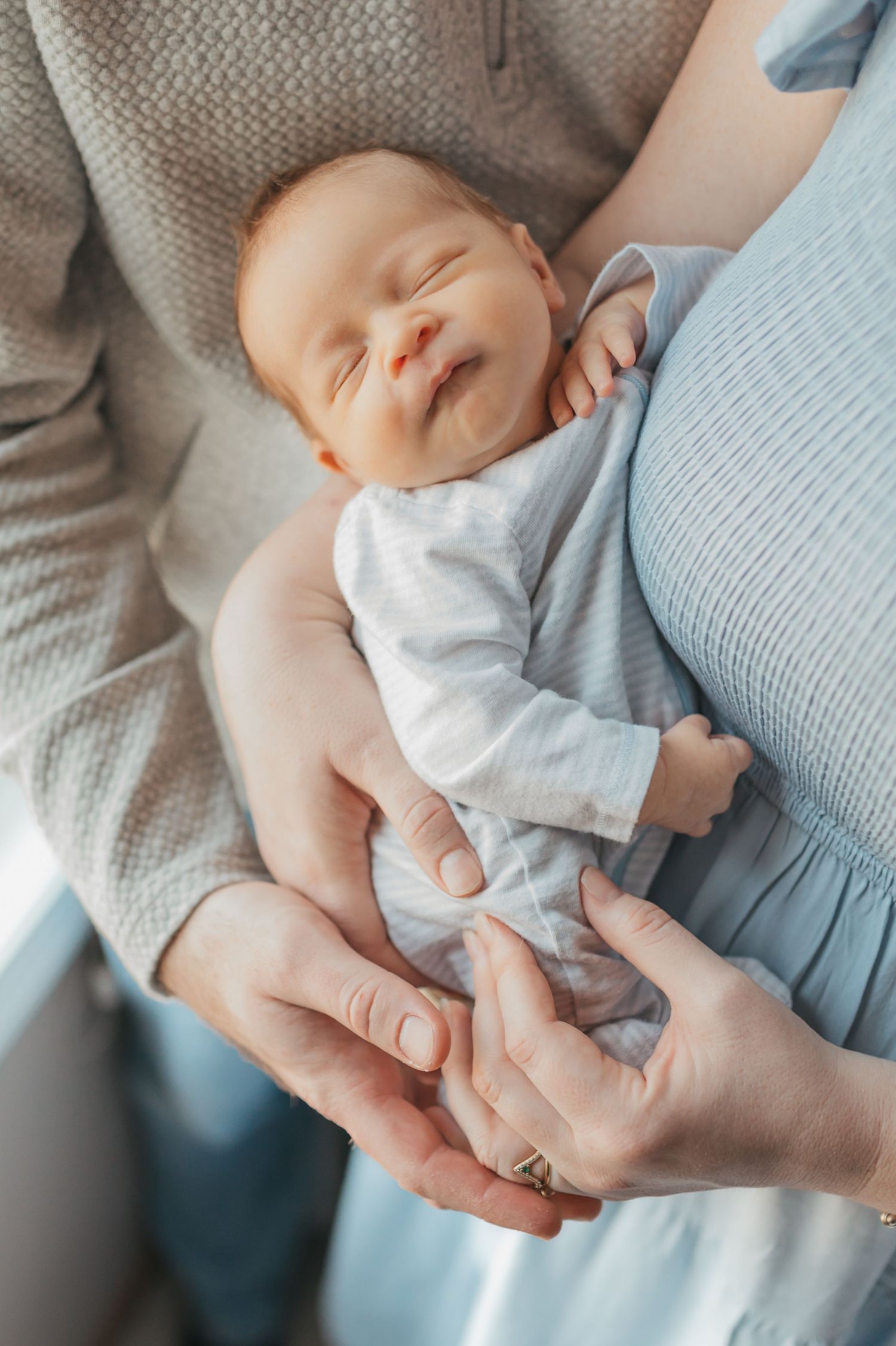 A sleeping newborn in light blue clothing being cradled in gentle hands.
