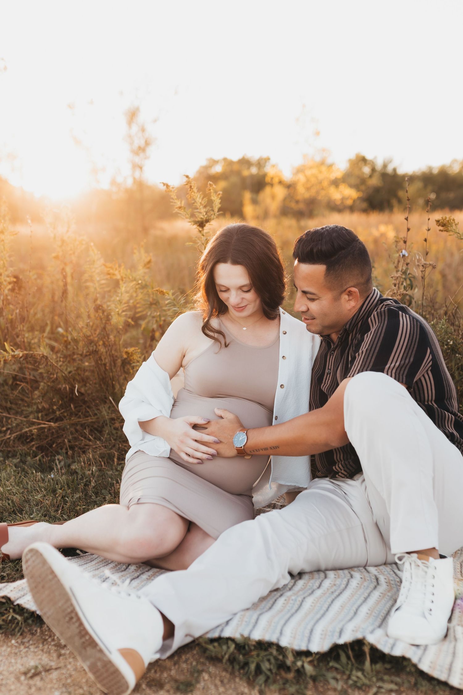 Tender maternity photos of couple laying in grass during sunset.