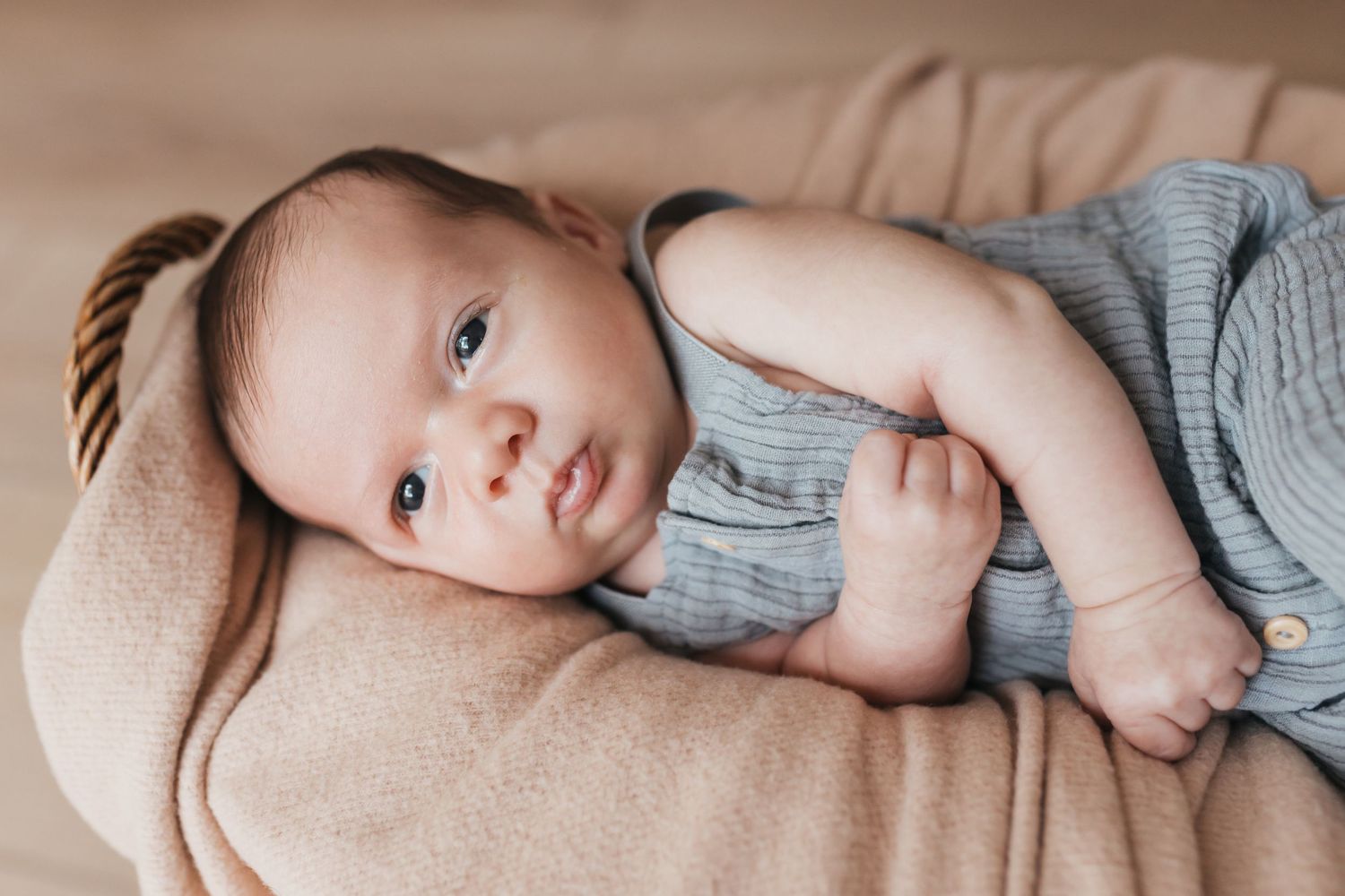 Baby in gray sweater resting on beige blanket.