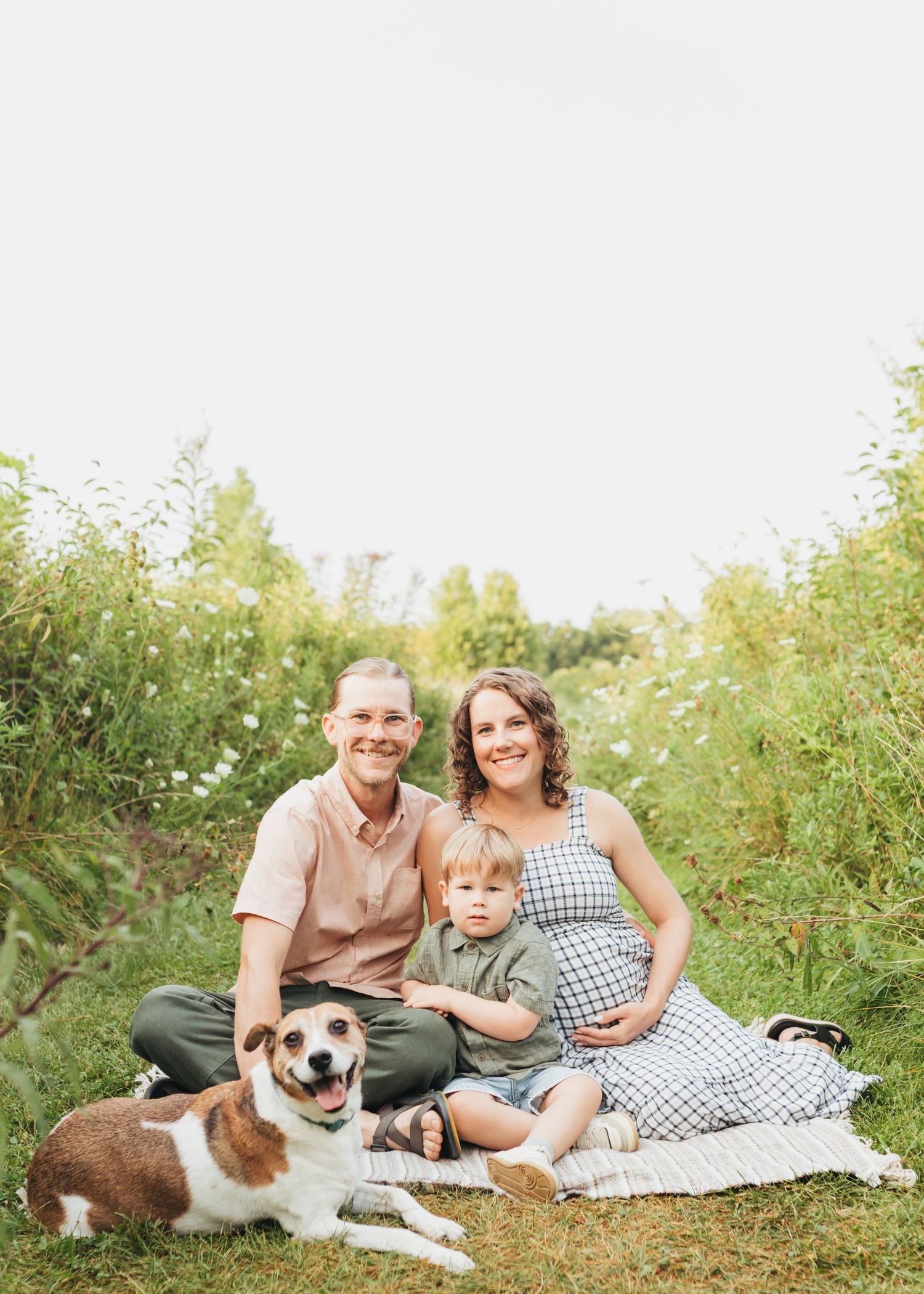 Family relaxes on a blanket in a sunny meadow with their dog enjoying a summer day.