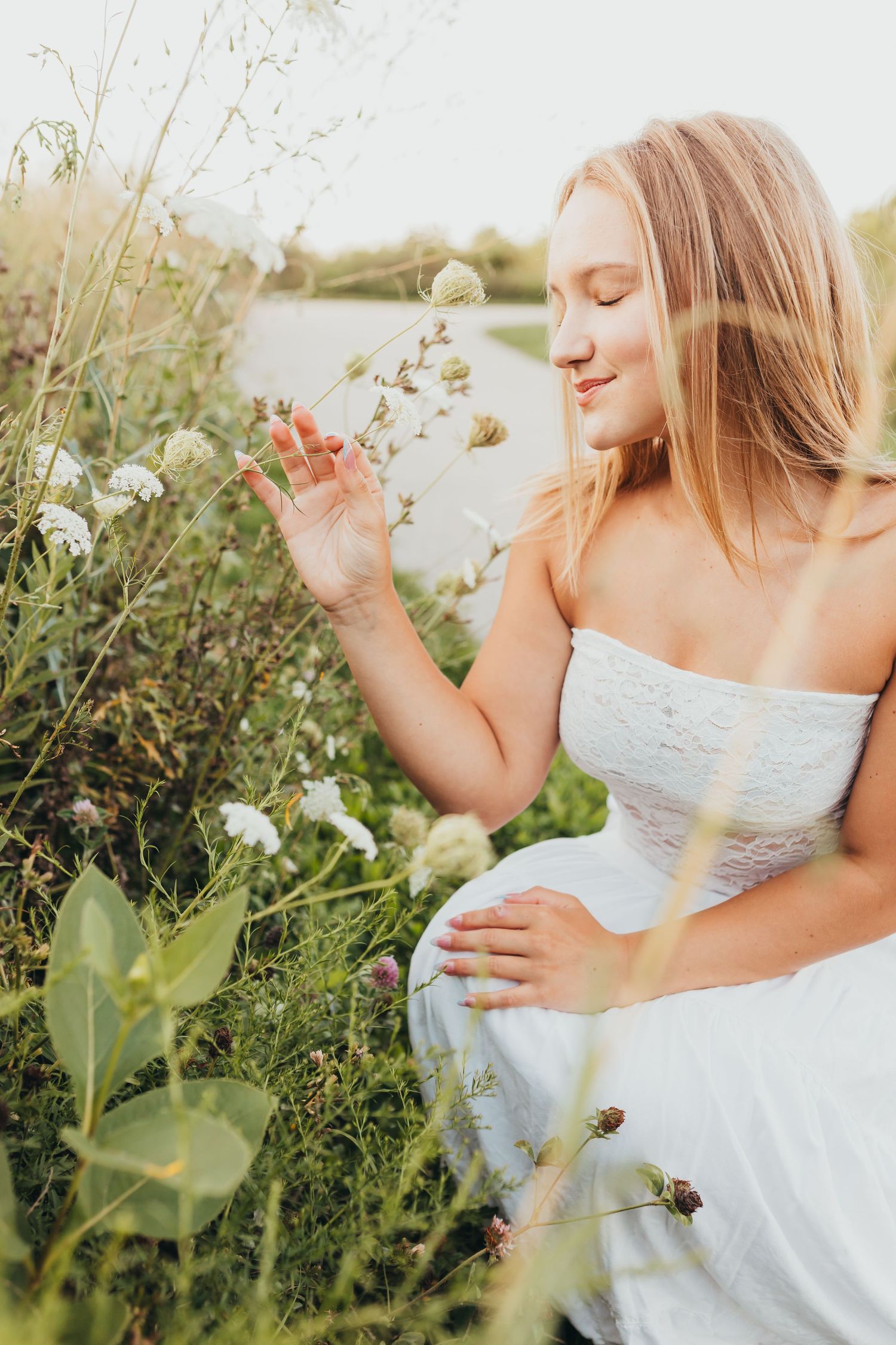 A dreamy portrait in a wildflower field with a woman in white touching delicate blooms.