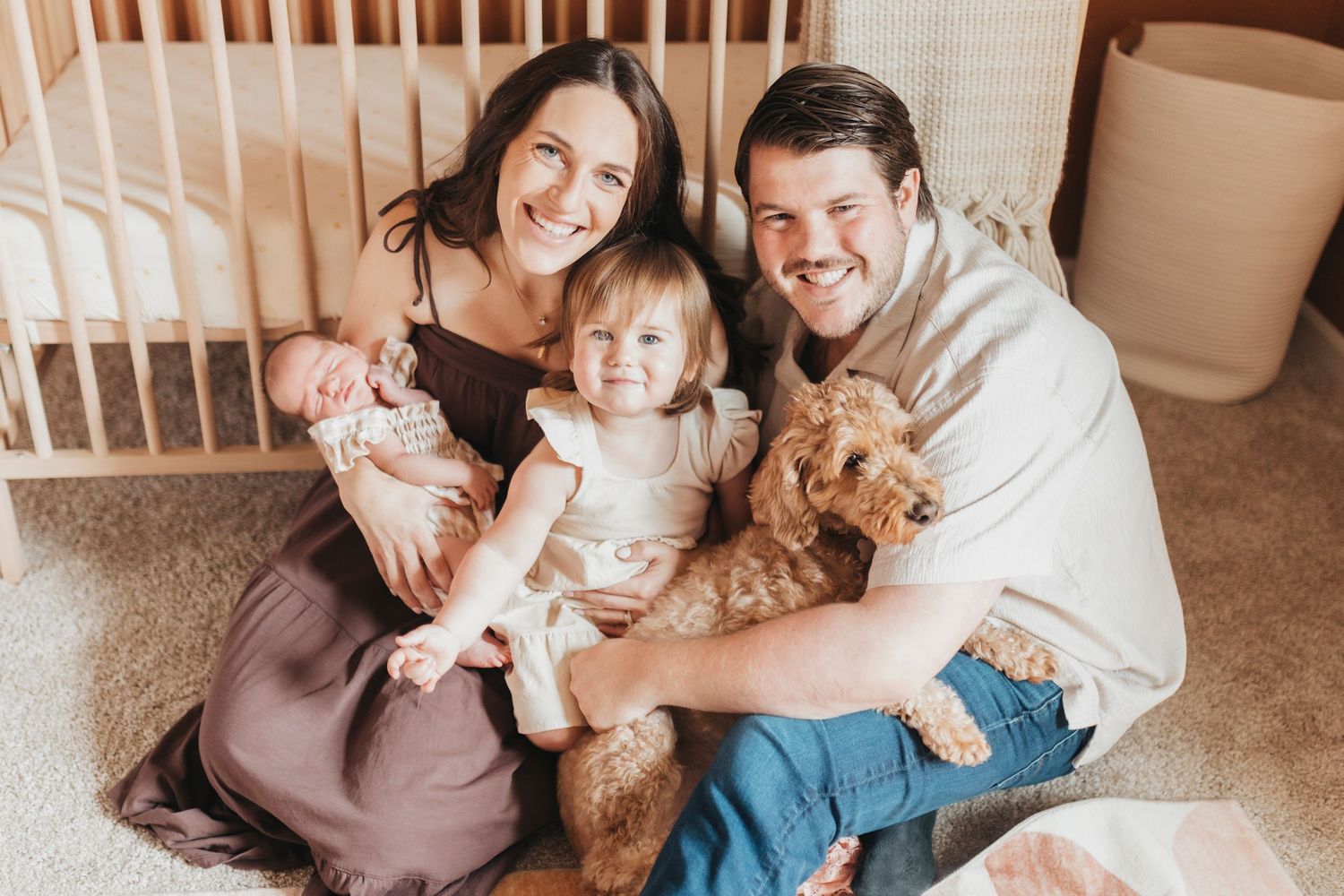 Family sitting together on carpet with wooden crib in background.
