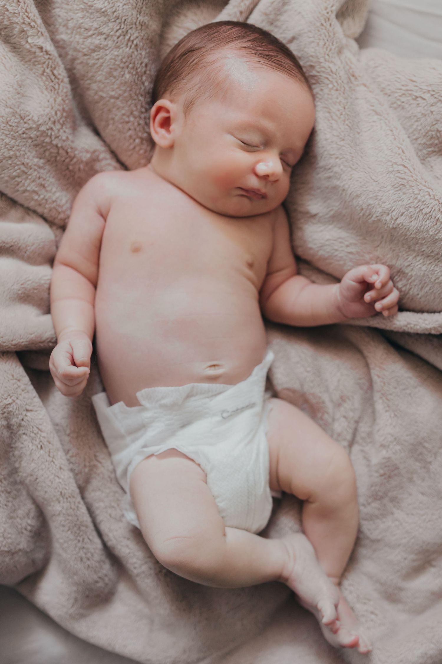 Sleeping newborn baby wearing white diaper on soft beige blanket.