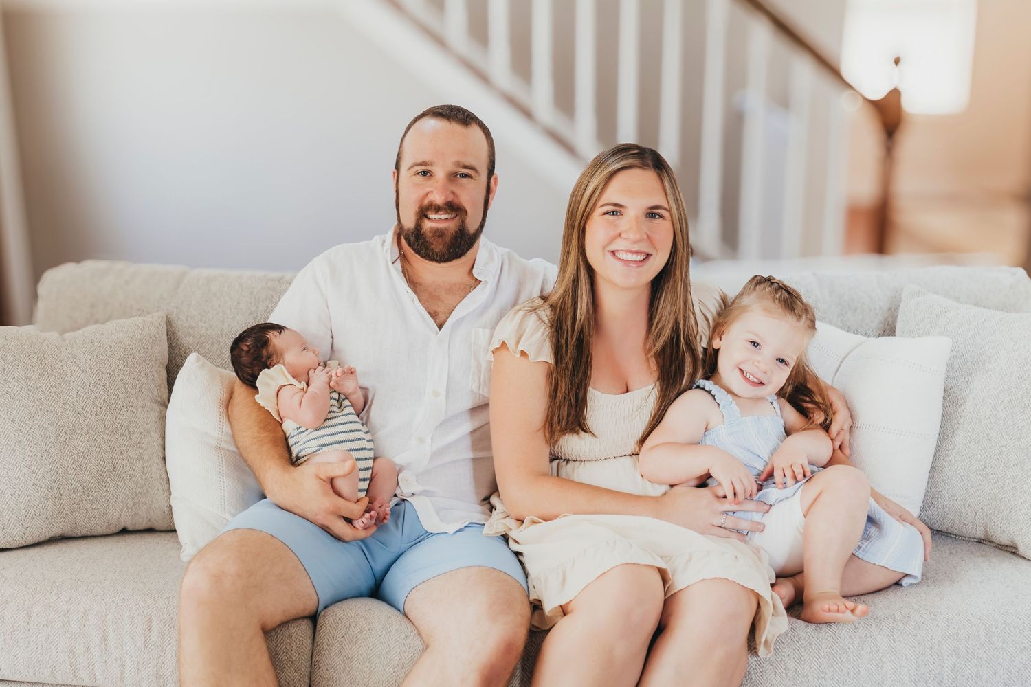 Family lying together on a cozy white couch during an intimate lifestyle photo session.