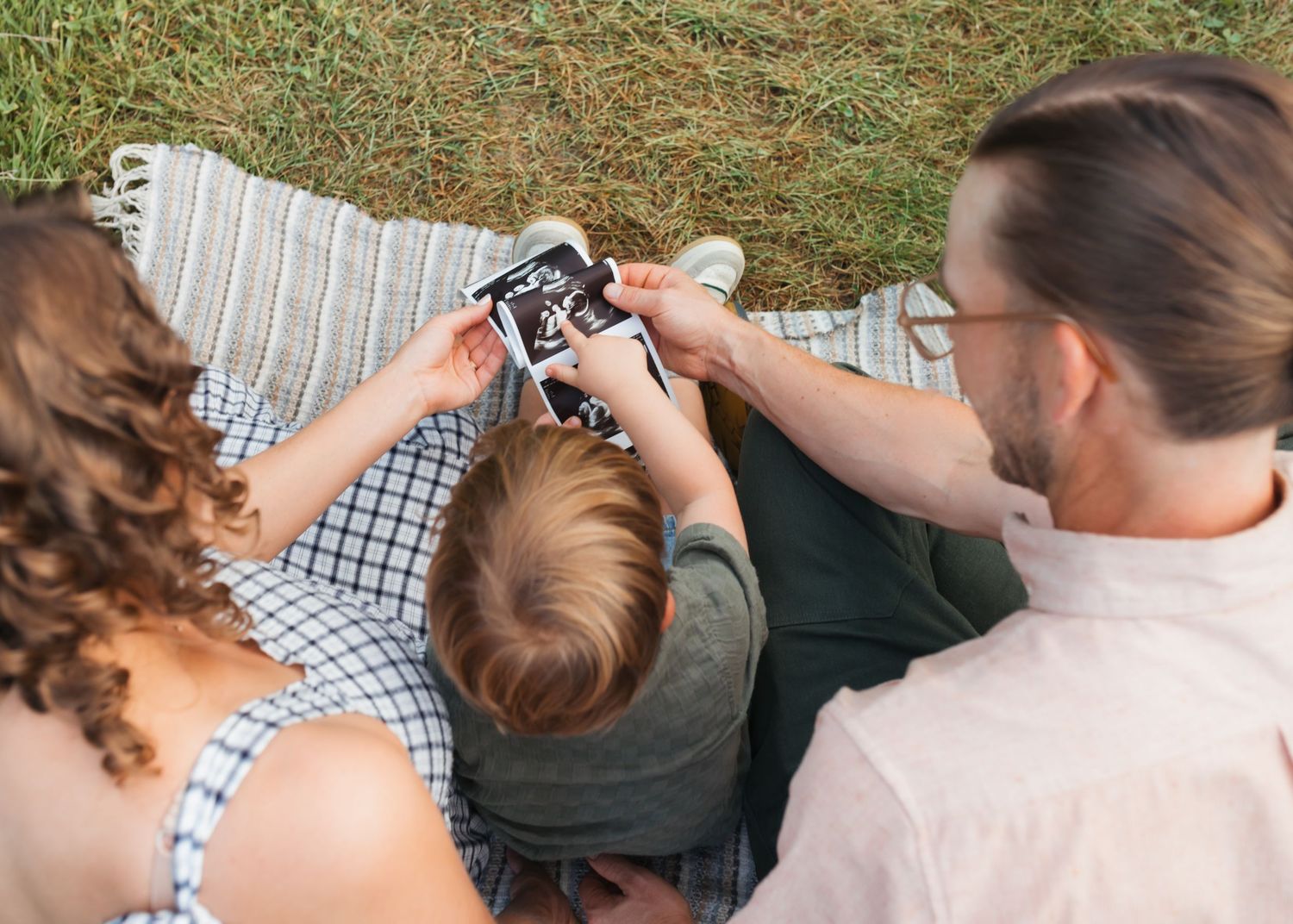 Family looking at photos together on a digital camera while sitting on a blanket outdoors.