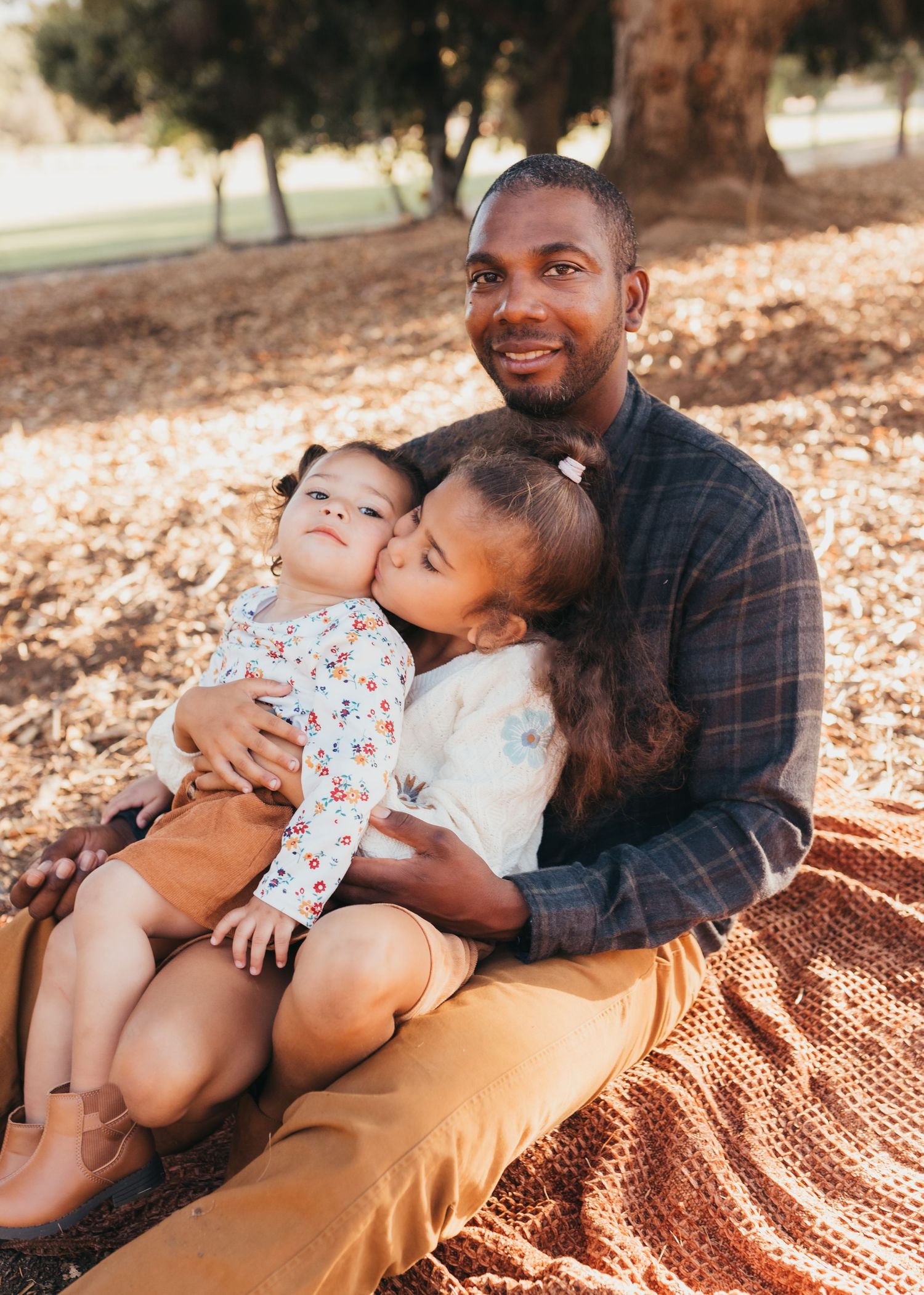 Family enjoying tender moments together on a cozy blanket in autumn sunlight.