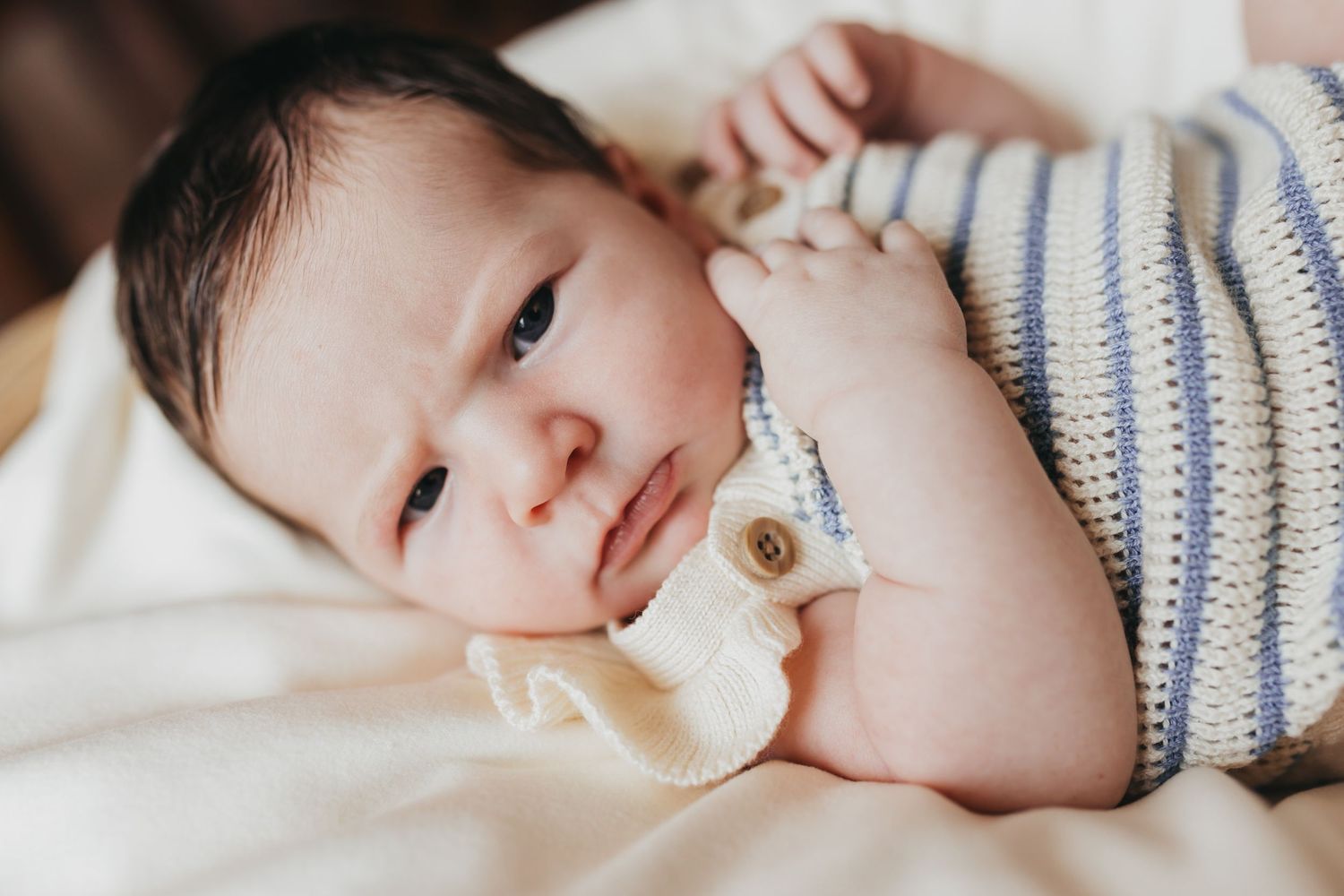 Sleeping newborn wearing striped hat in soft natural lighting.