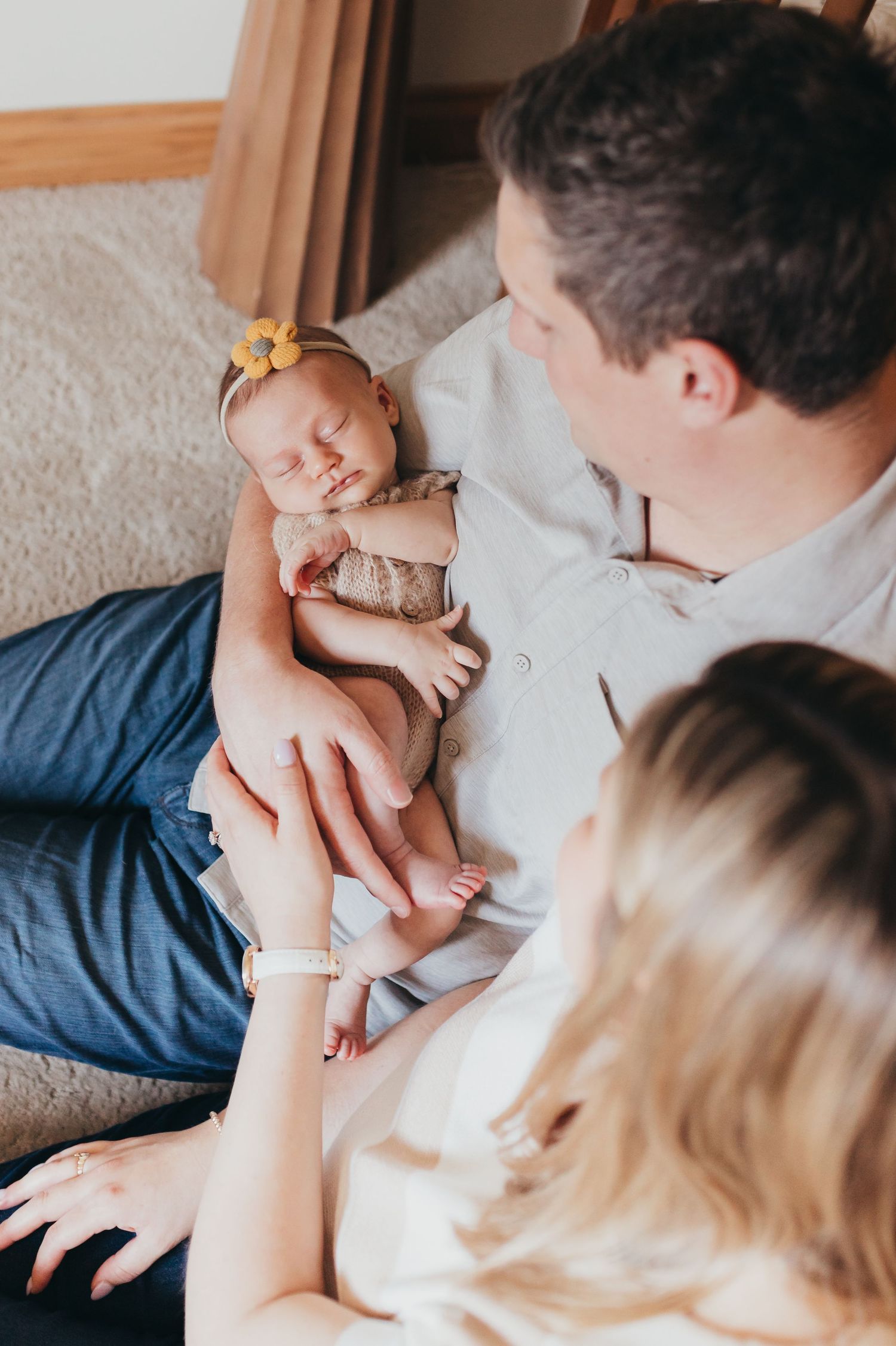 Parents snuggling with newborn baby on grey couch during lifestyle session.