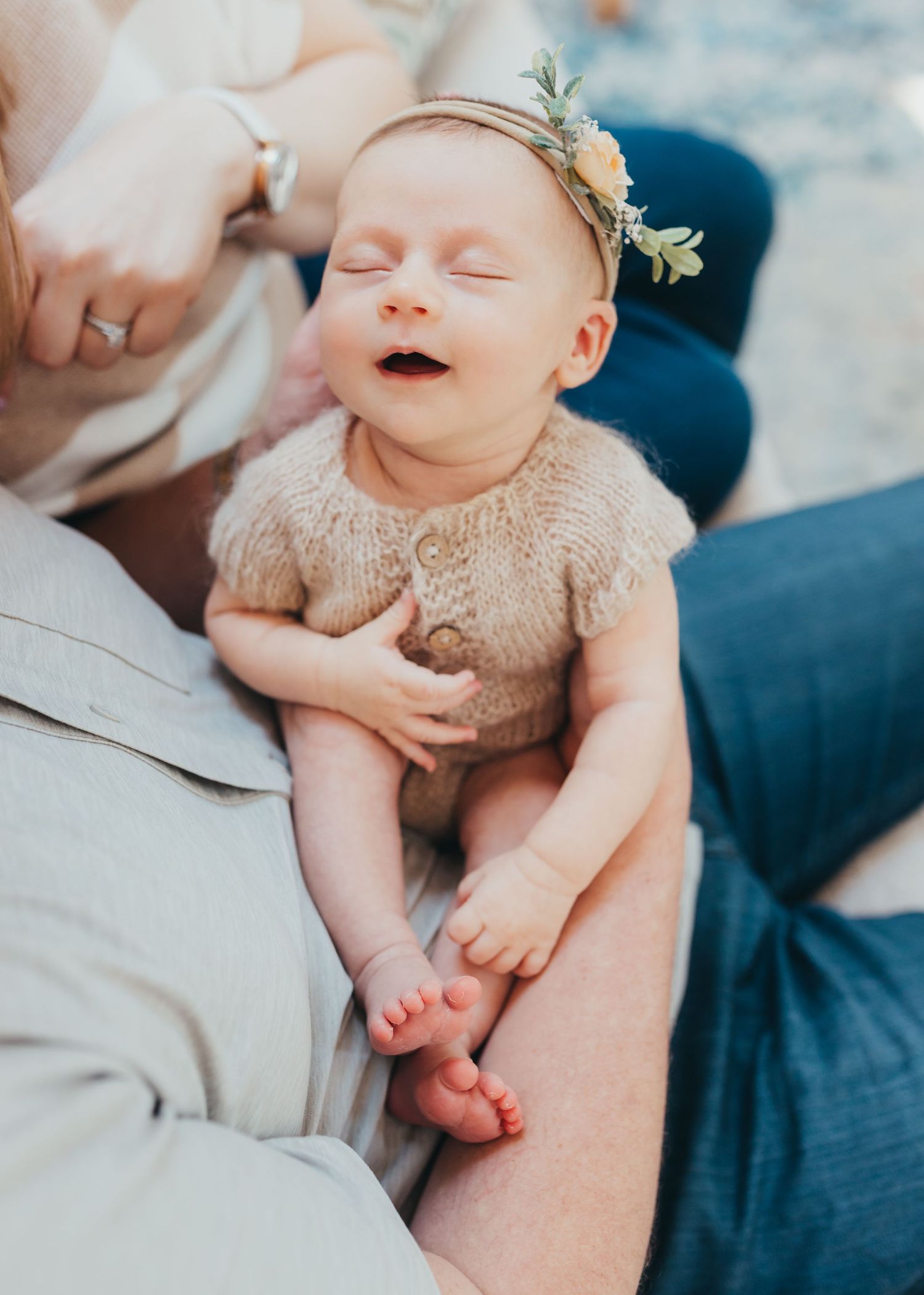 Newborn baby in beige outfit smiling during lifestyle photo session.