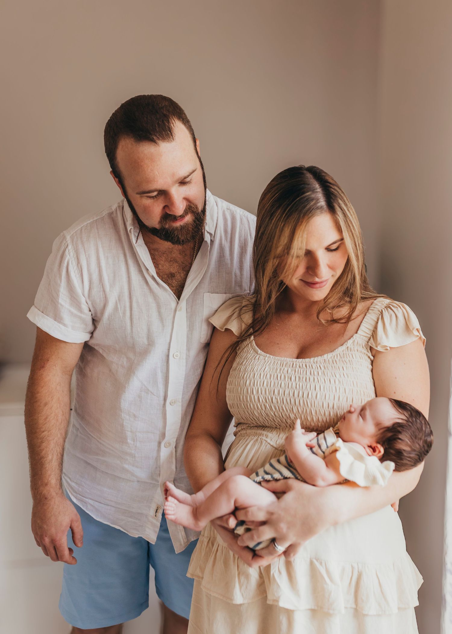Couple in white clothing sharing tender moments with their newborn in natural light setting.