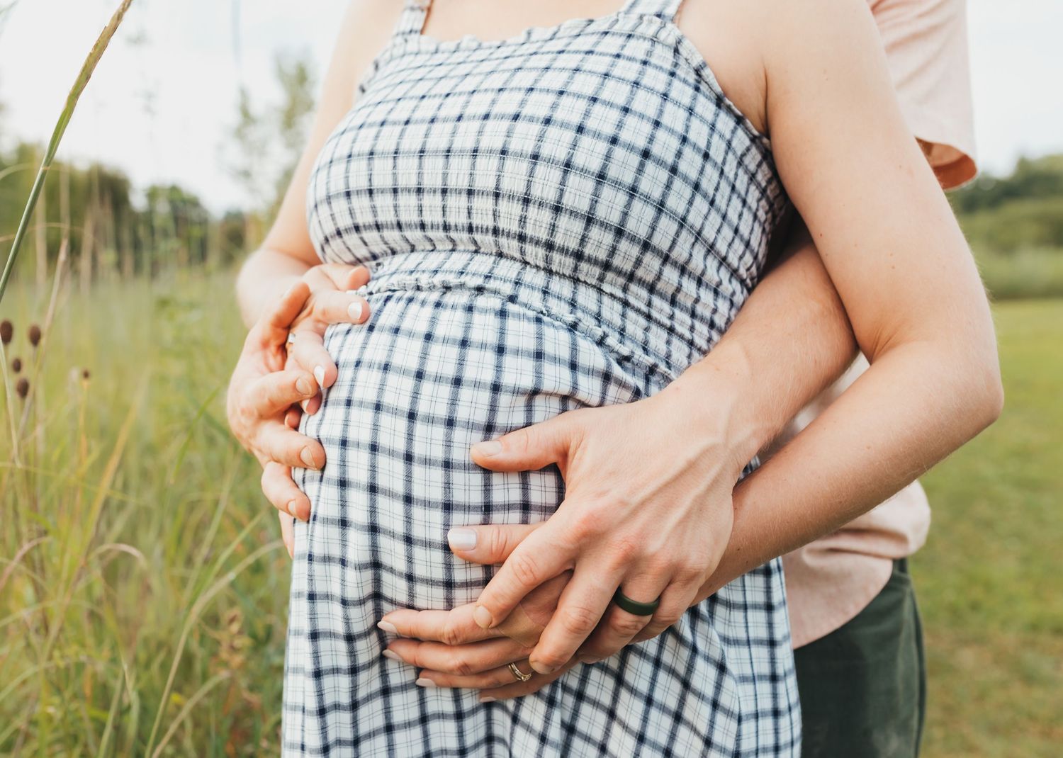 Close-up of hands cradling a pregnant belly in a checkered dress.