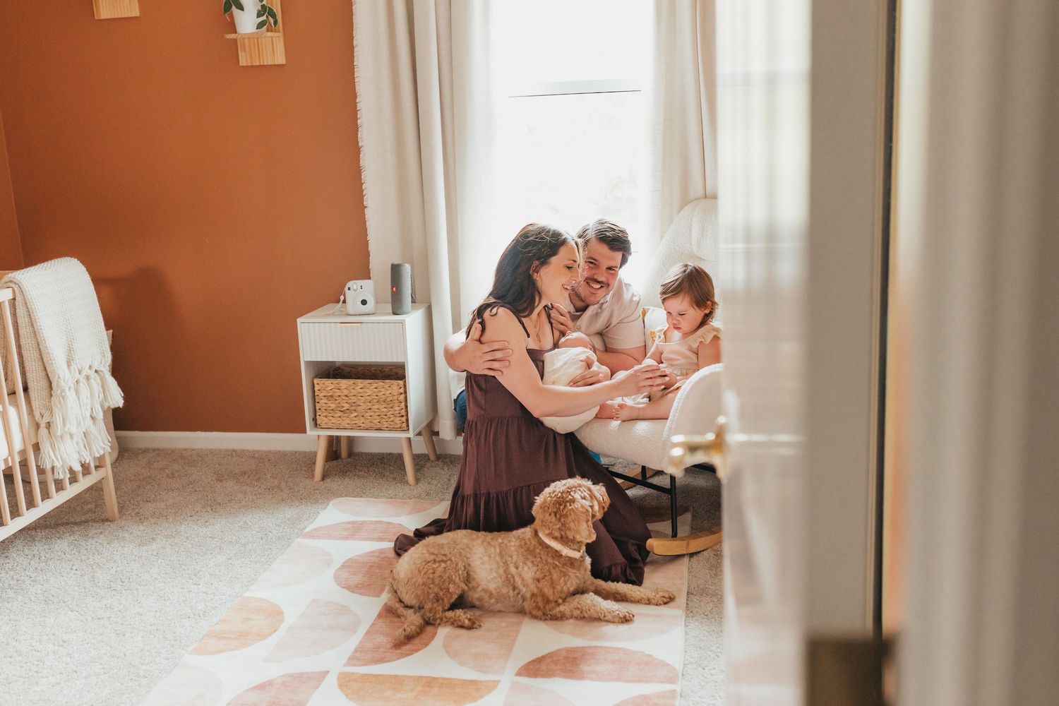 Tender family moment captured in a cozy nursery with white carpet and orange walls.