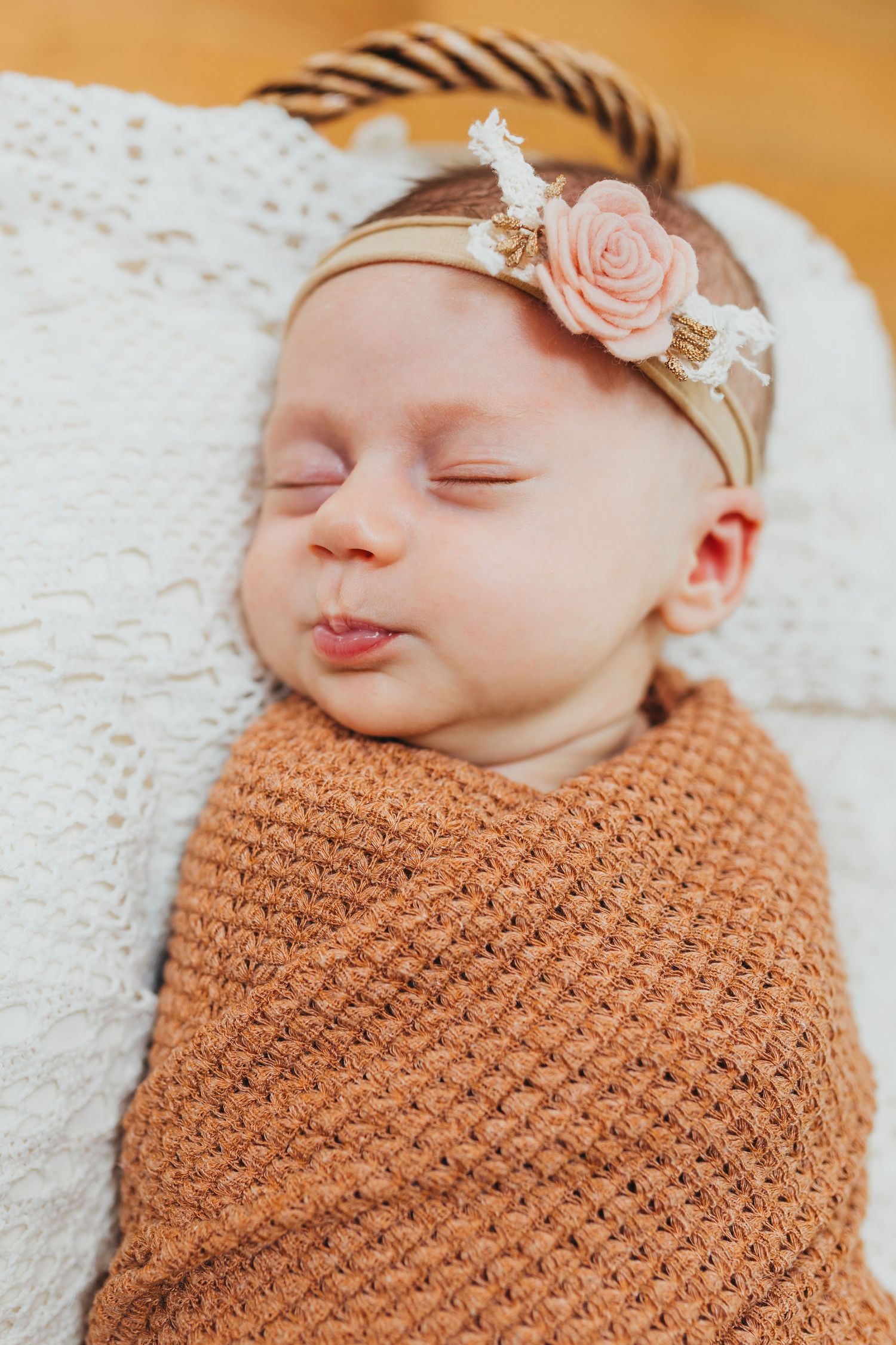 Sleeping newborn wrapped in brown knit blanket wearing delicate floral headband.