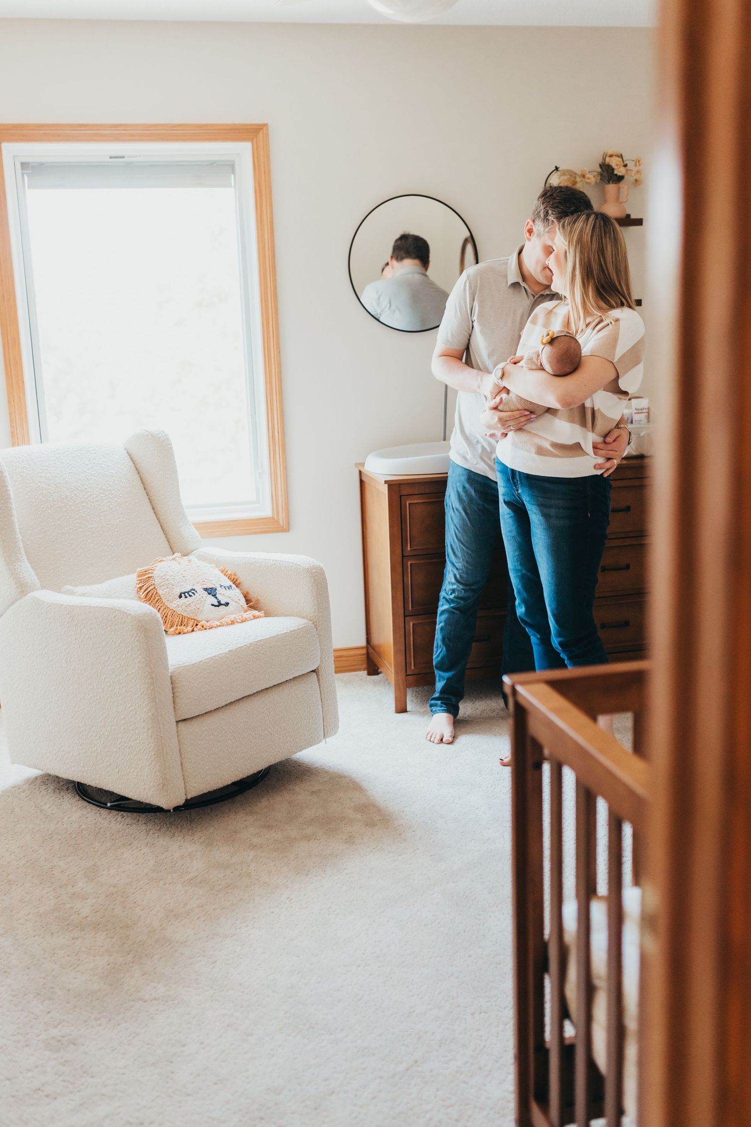 Parents walking with baby in nursery with white rocking chair and natural light.