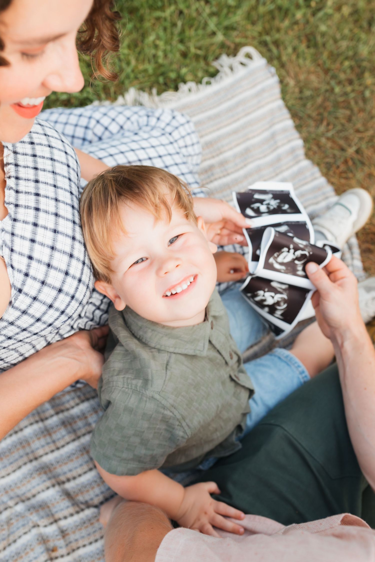Candid moments of joy and laughter while looking at ultrasound photos on a picnic blanket.