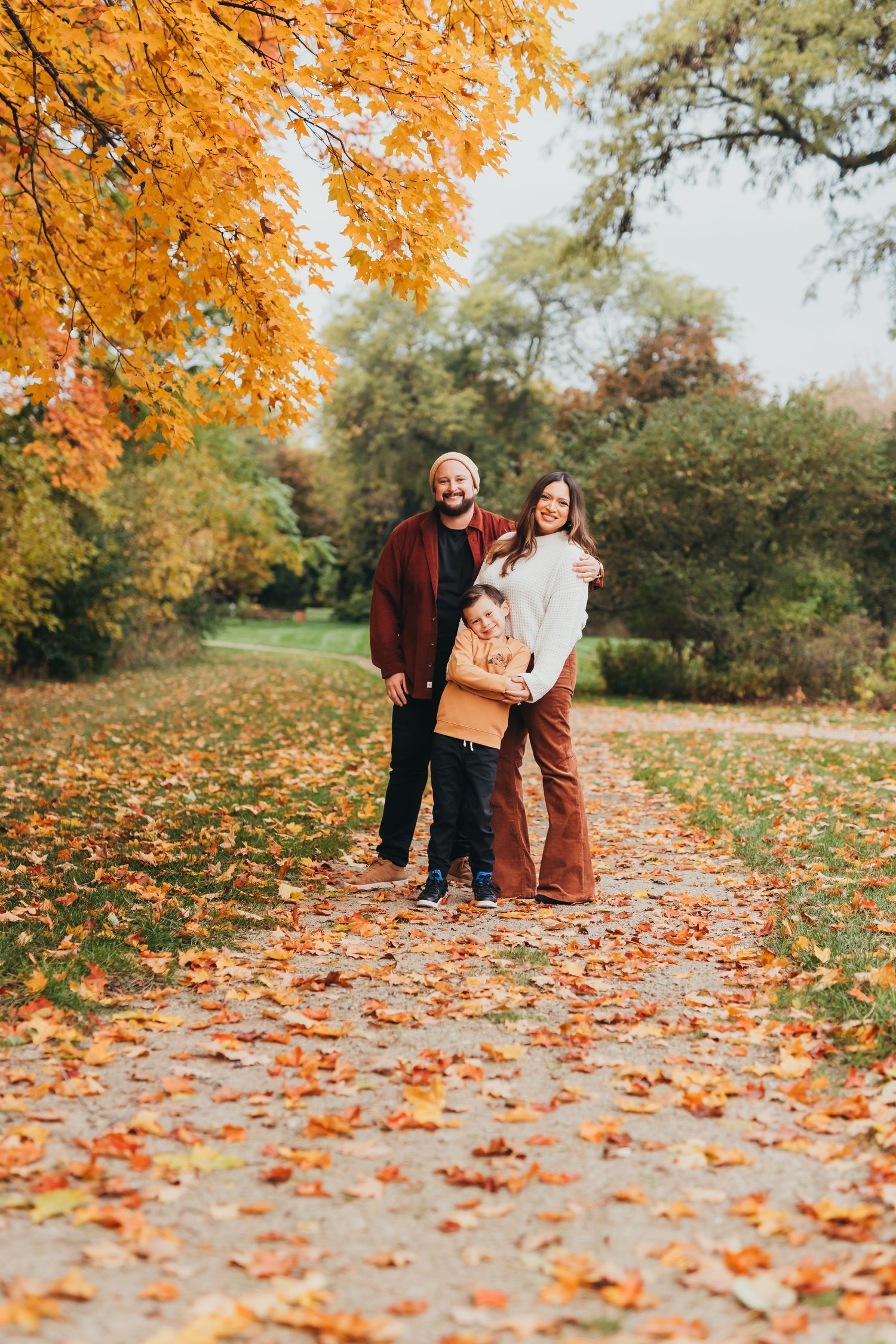A family walks together on a path covered in vibrant orange autumn leaves during a fall photoshoot in the park.