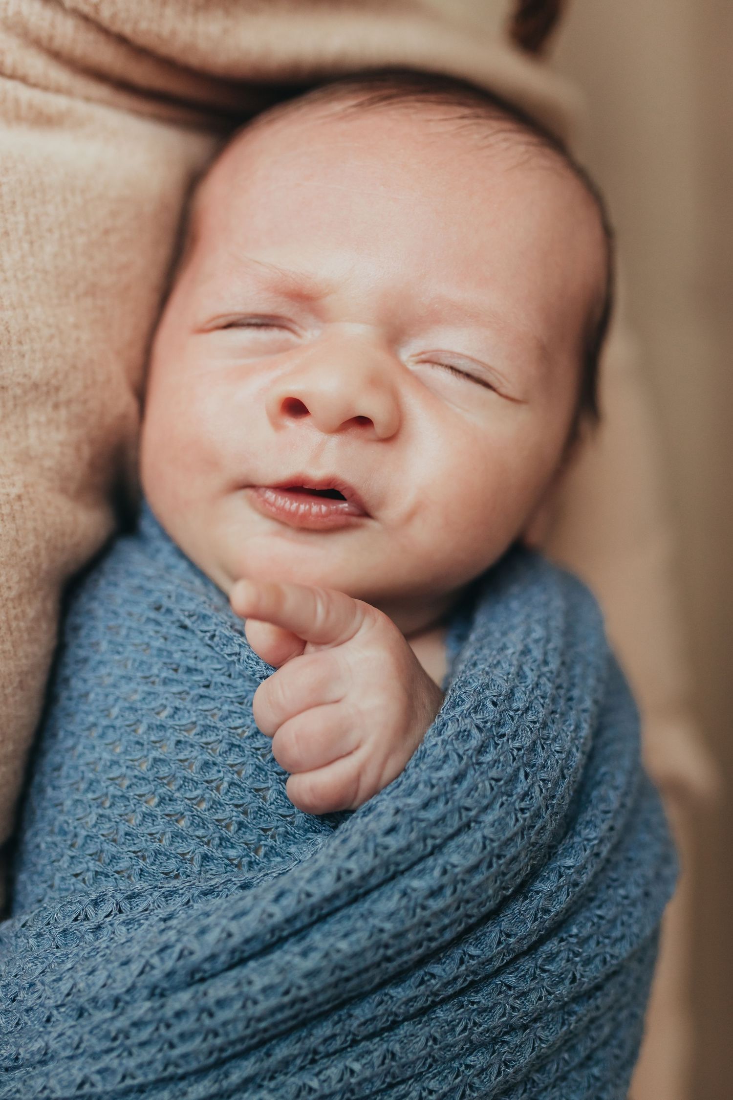Peaceful newborn wrapped in blue knit blanket with gentle smile.