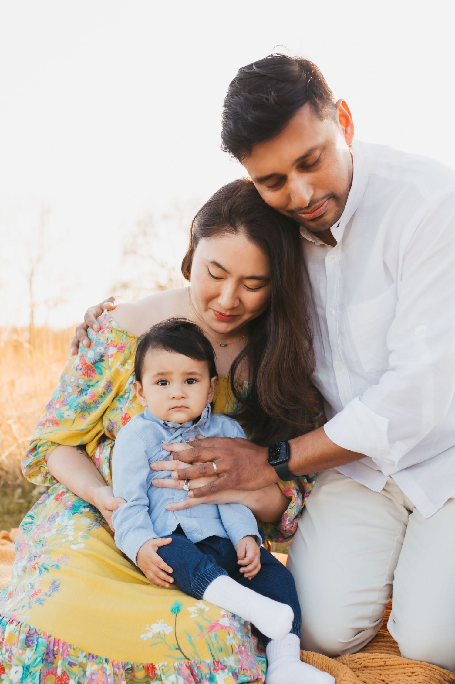 Family sitting together outdoors during golden hour in casual attire.