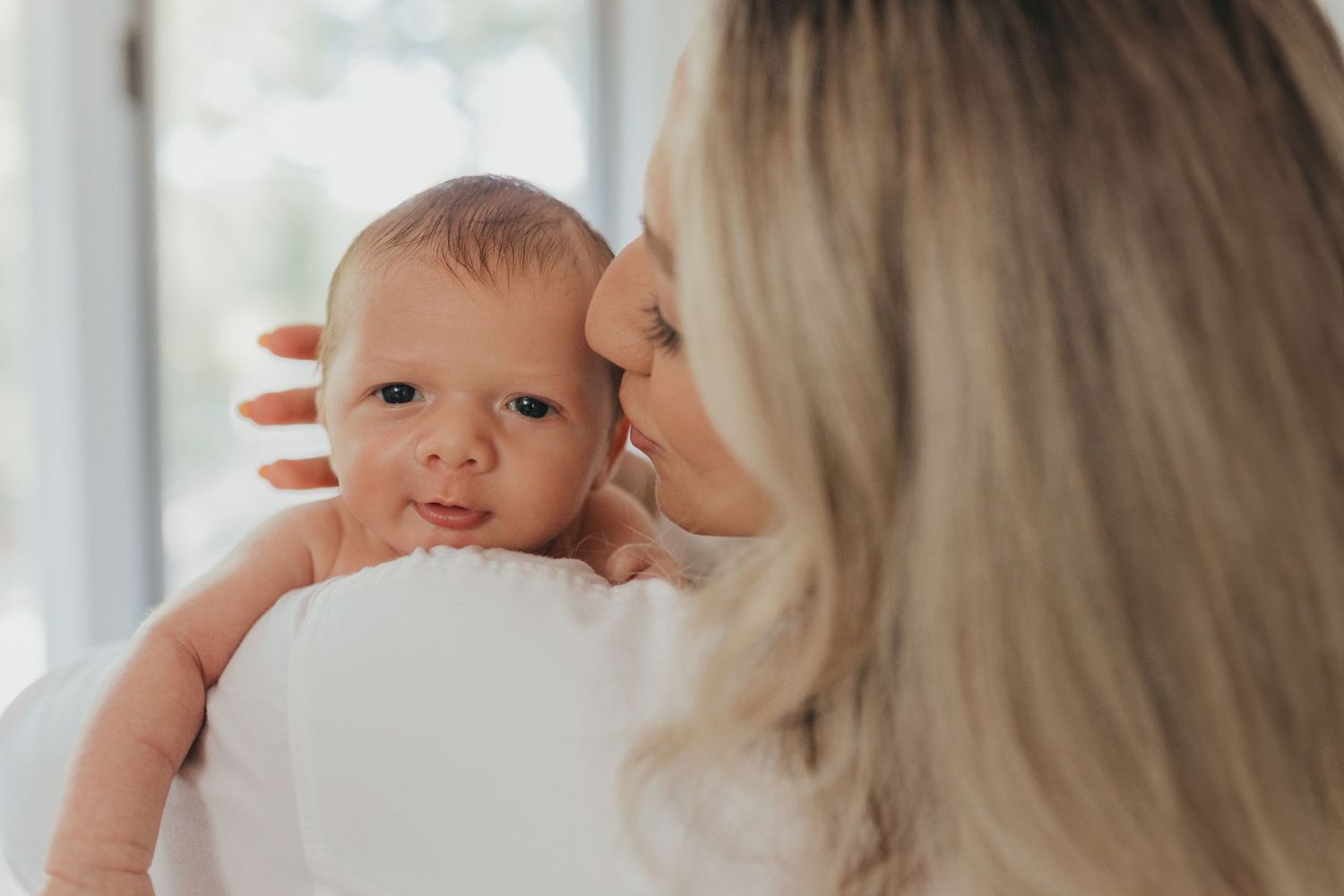 Tender moment between parent and baby in bright natural light setting.