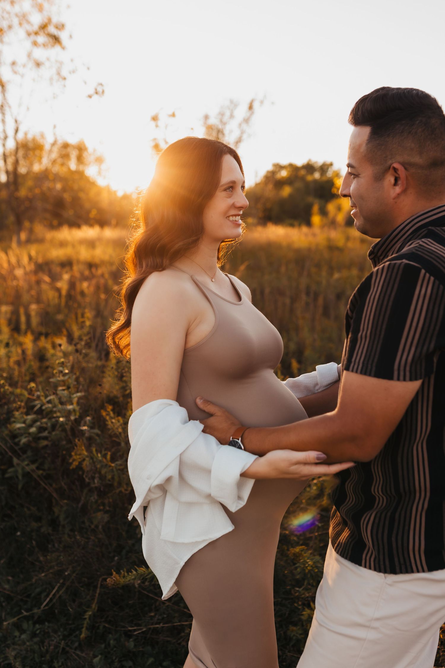 A couple embraces in a golden sunset field during a romantic maternity photoshoot.