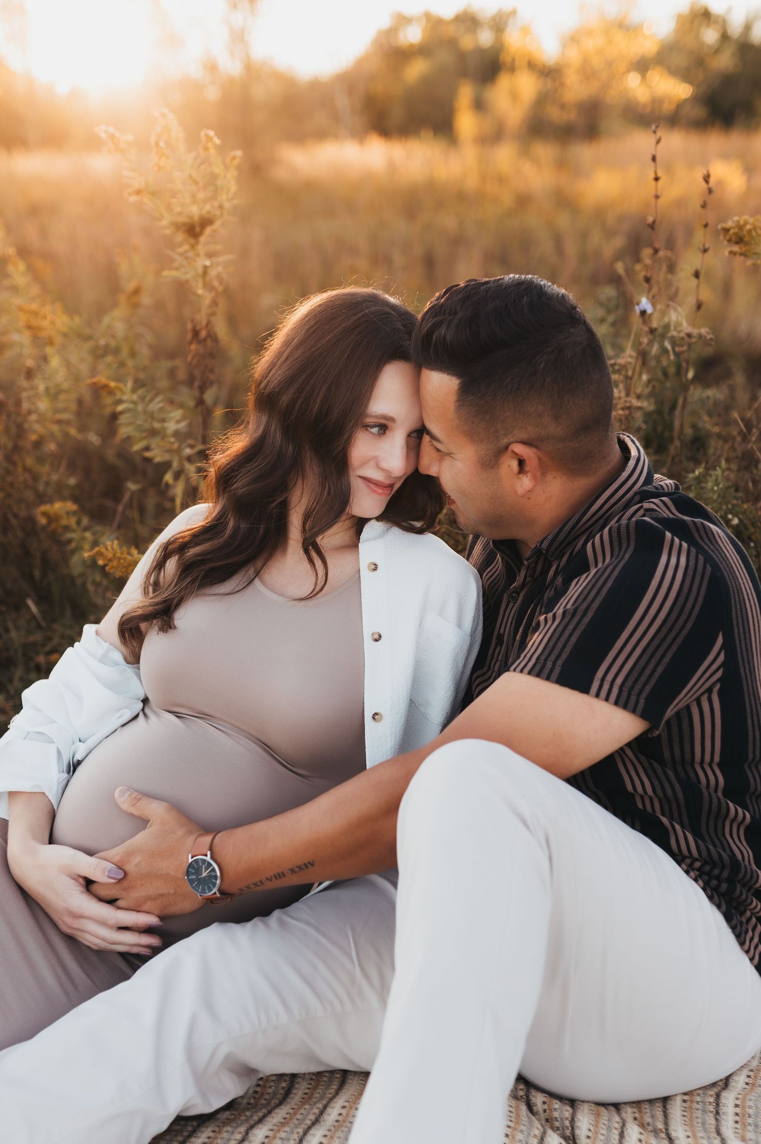 Intimate maternity photo of couple embracing in golden sunlit field at sunset during pregnancy photoshoot.