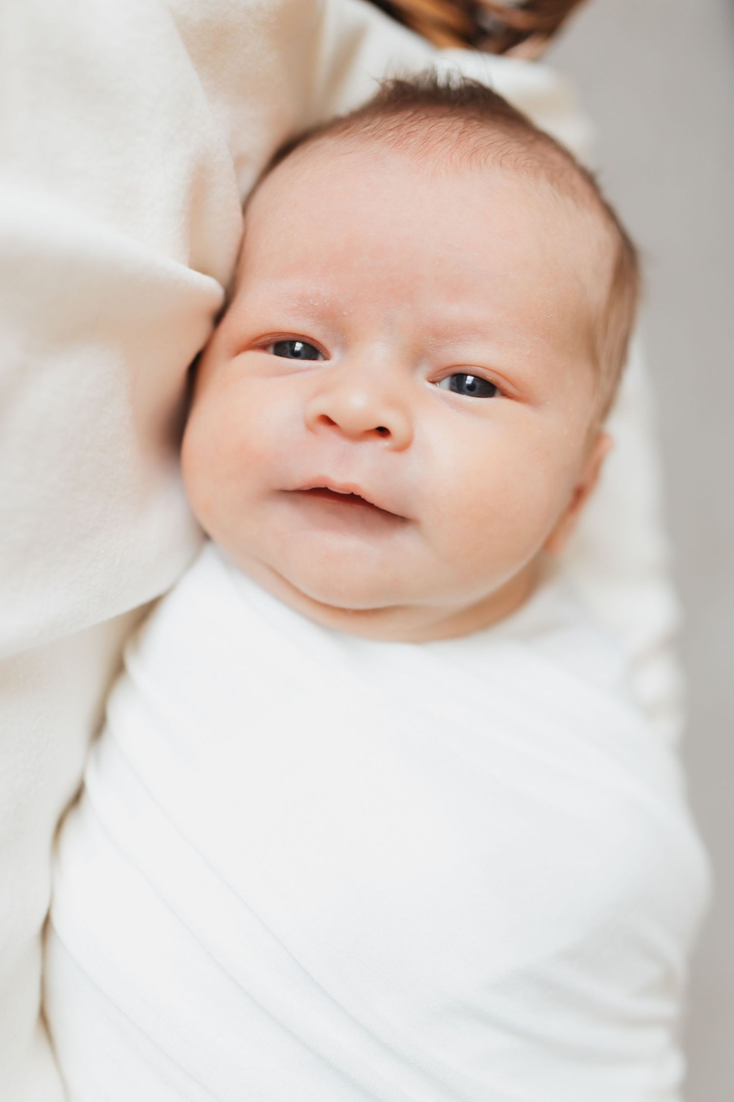 A sweet close-up of a baby in white clothing with bright eyes and a gentle expression.