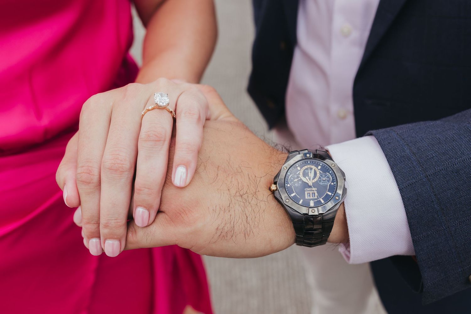 Elegant engagement ring detail shot with hands against formal attire.