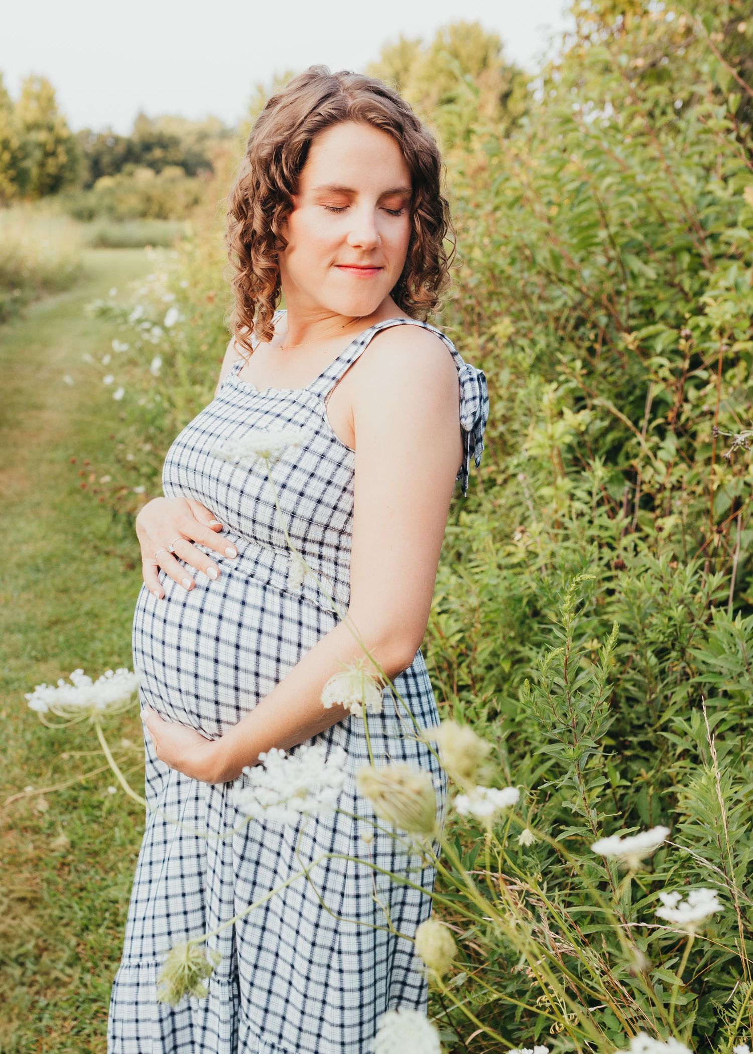 Woman in checkered dress standing among wildflowers in a summer field.