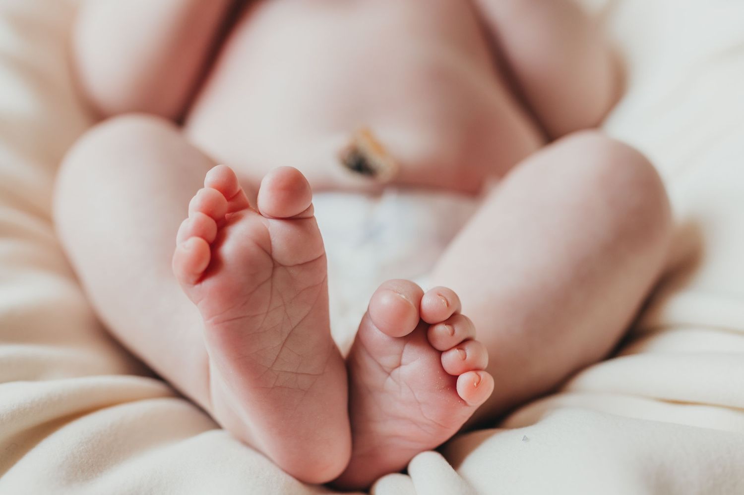 Close-up of tiny newborn baby feet on white bedding.