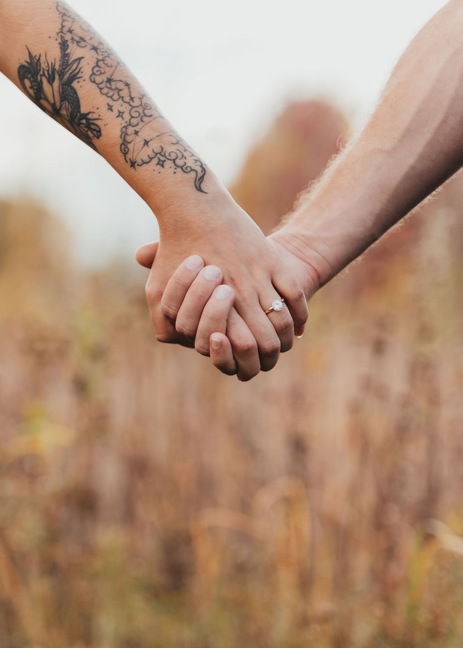 Tattooed hands intertwined against a backdrop of autumn foliage.