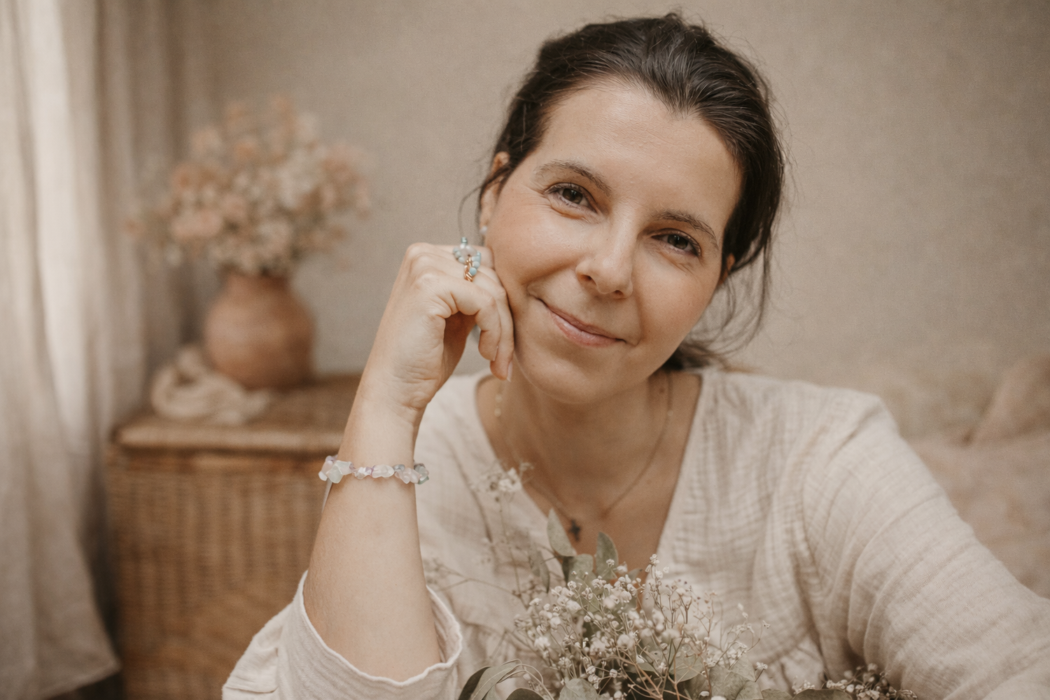 Warm toned portrait of someone in a cream sweater holding dried flowers while resting their head on their hand.