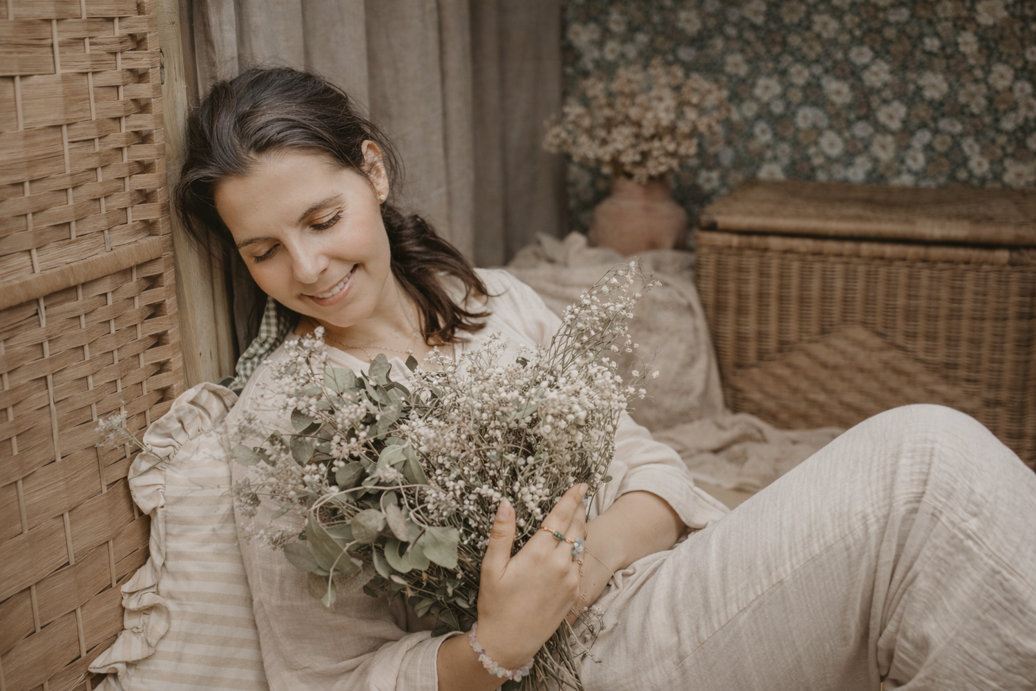 A bride in a white lace wedding dress holds a delicate bouquet of baby's breath flowers against a brick wall.