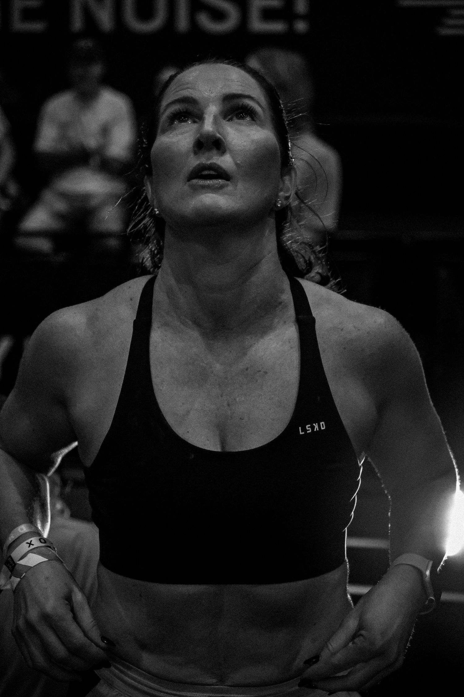 Black and white photo of a focused female athlete in a sports bra looking up during a CrossFit competition.
