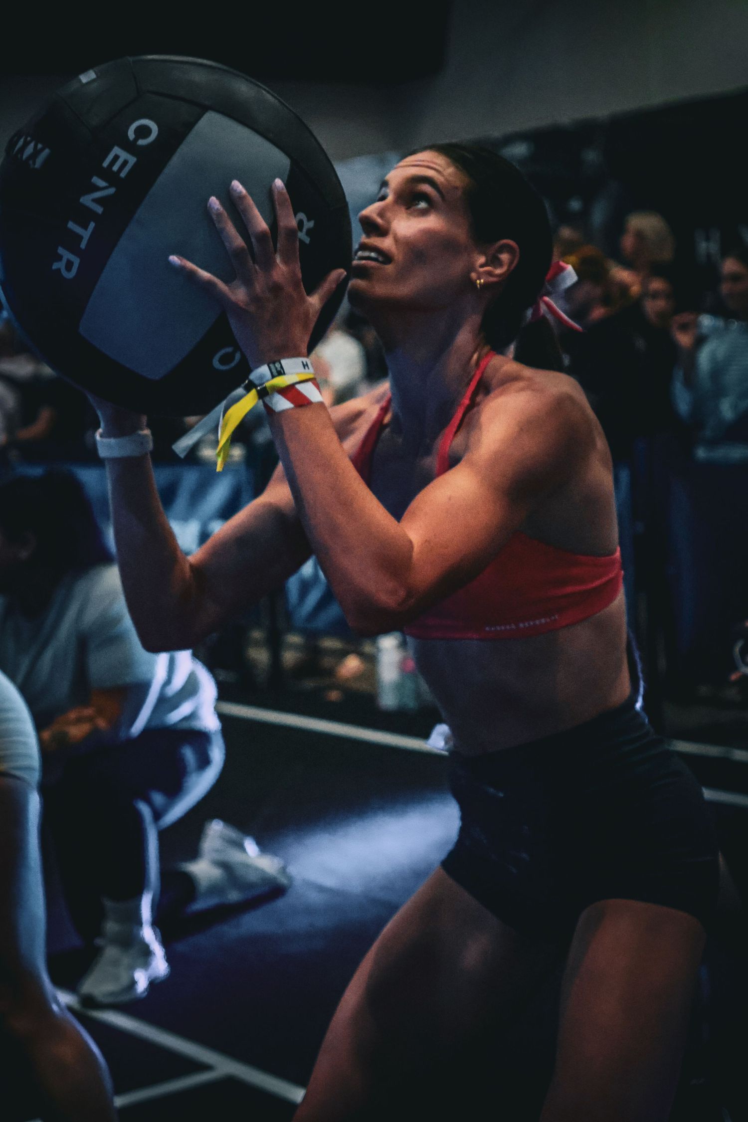 Woman in red sports bra lifting a medicine ball during an intense gym workout competition.