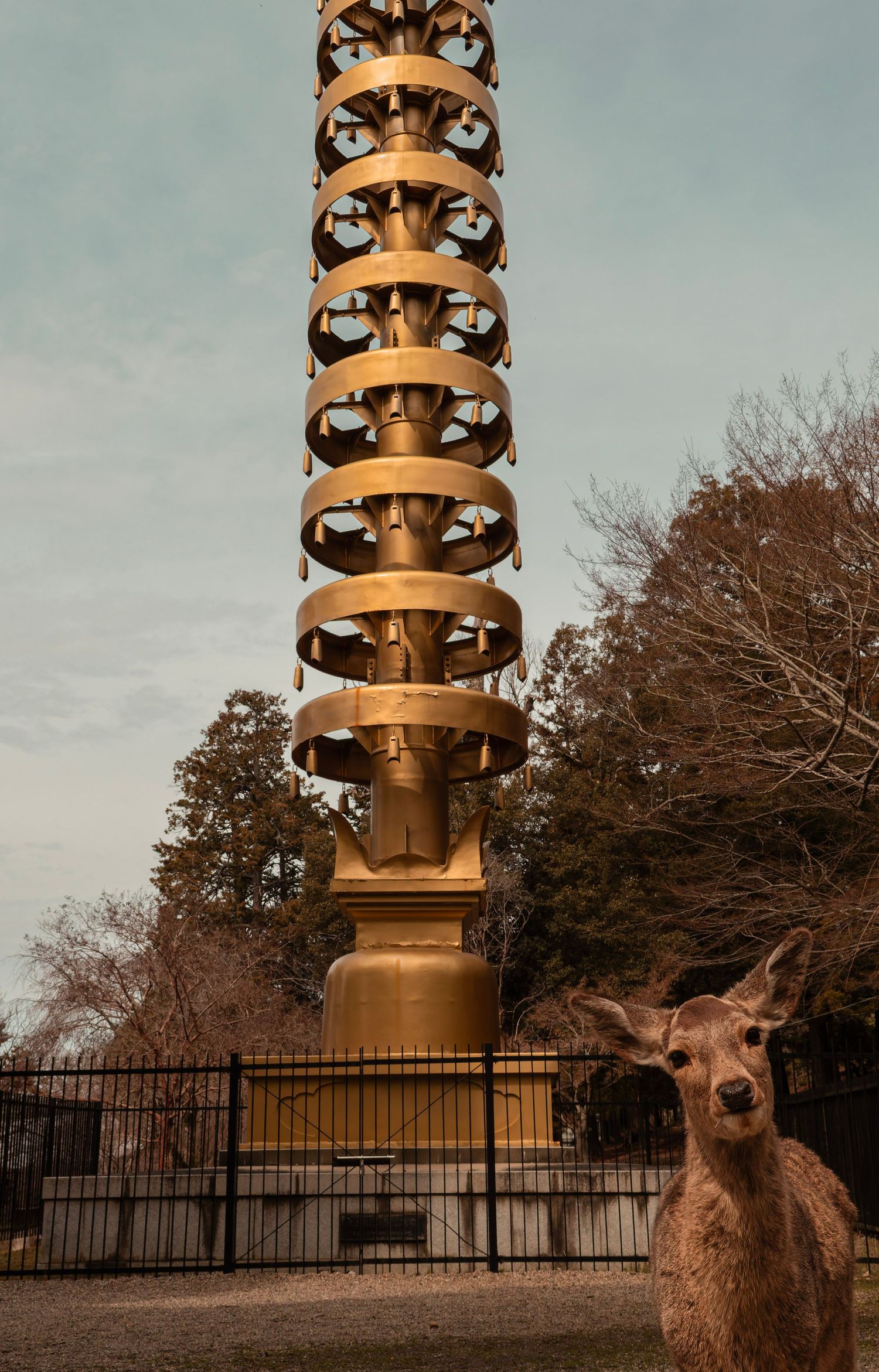 A deer stands before a tall golden bronze lantern tower at a Japanese shrine at dusk.
