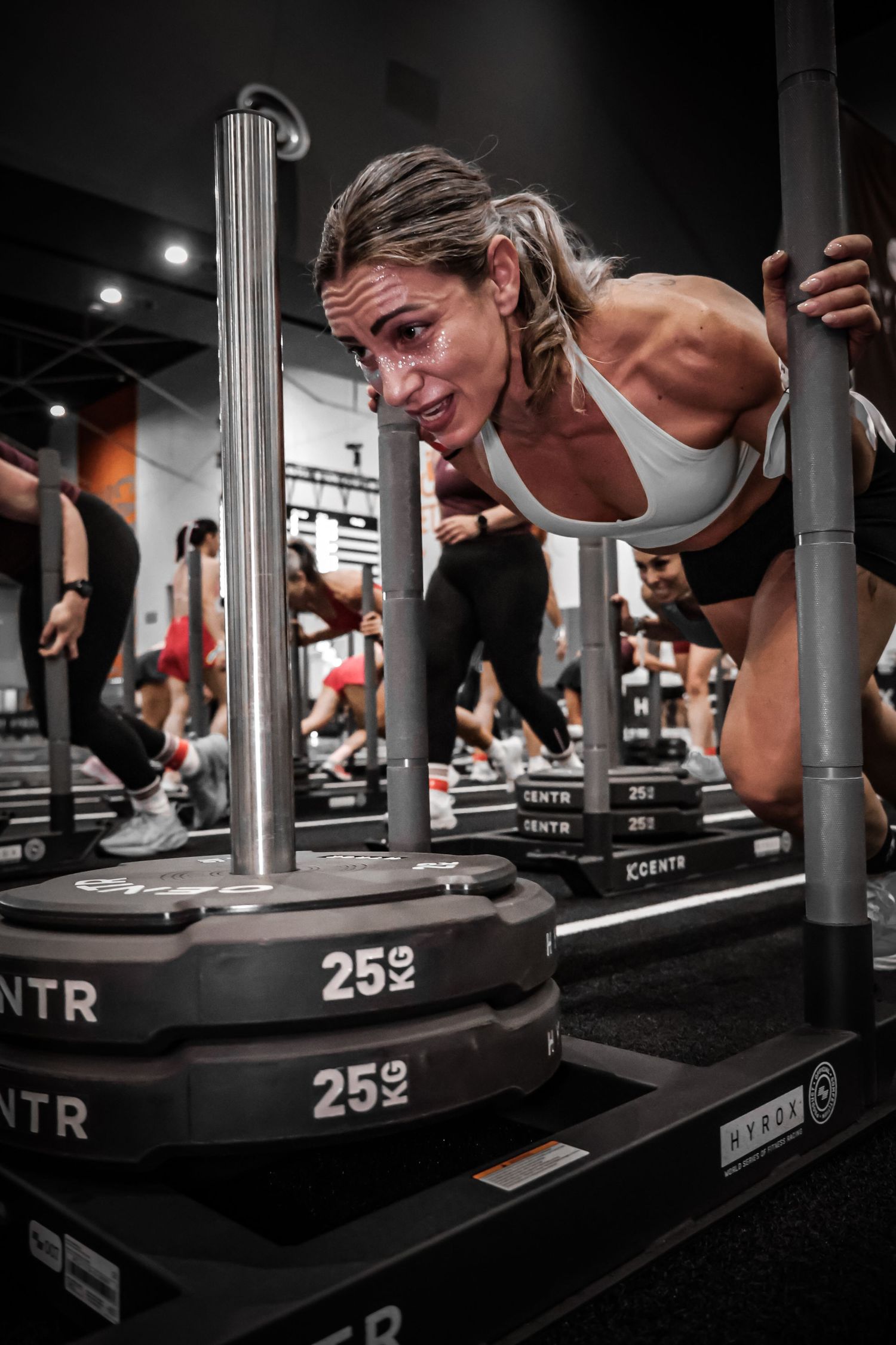 Woman pushing a weighted CENTR sled in a group fitness class at a modern gym.