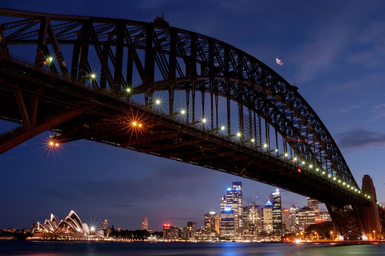 Sydney Harbour Bridge illuminated at dusk above the Opera House and city skyline, Australia.