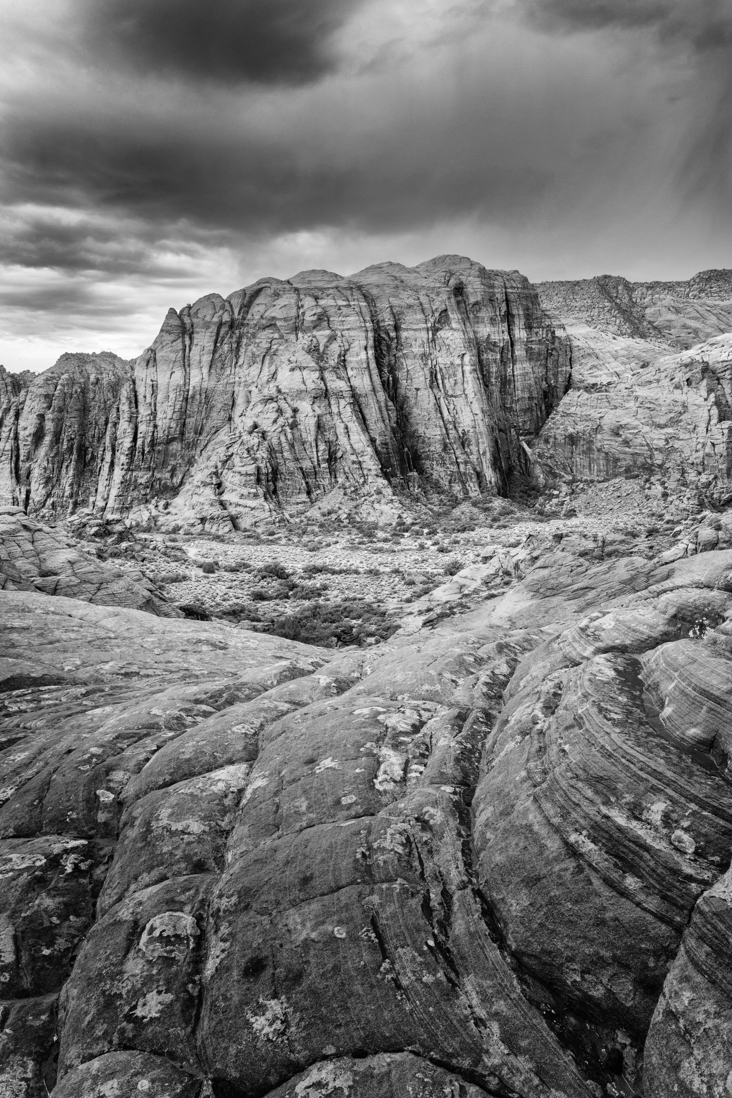 Black-and-white view of a rugged mountain valley beneath dramatic storm clouds.