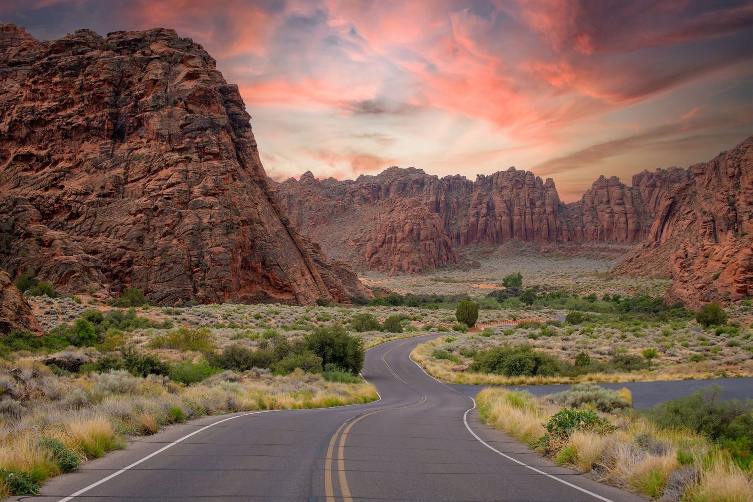 Winding road through red-rock cliffs beneath a colorful sunset in Snow Canyon, Utah.