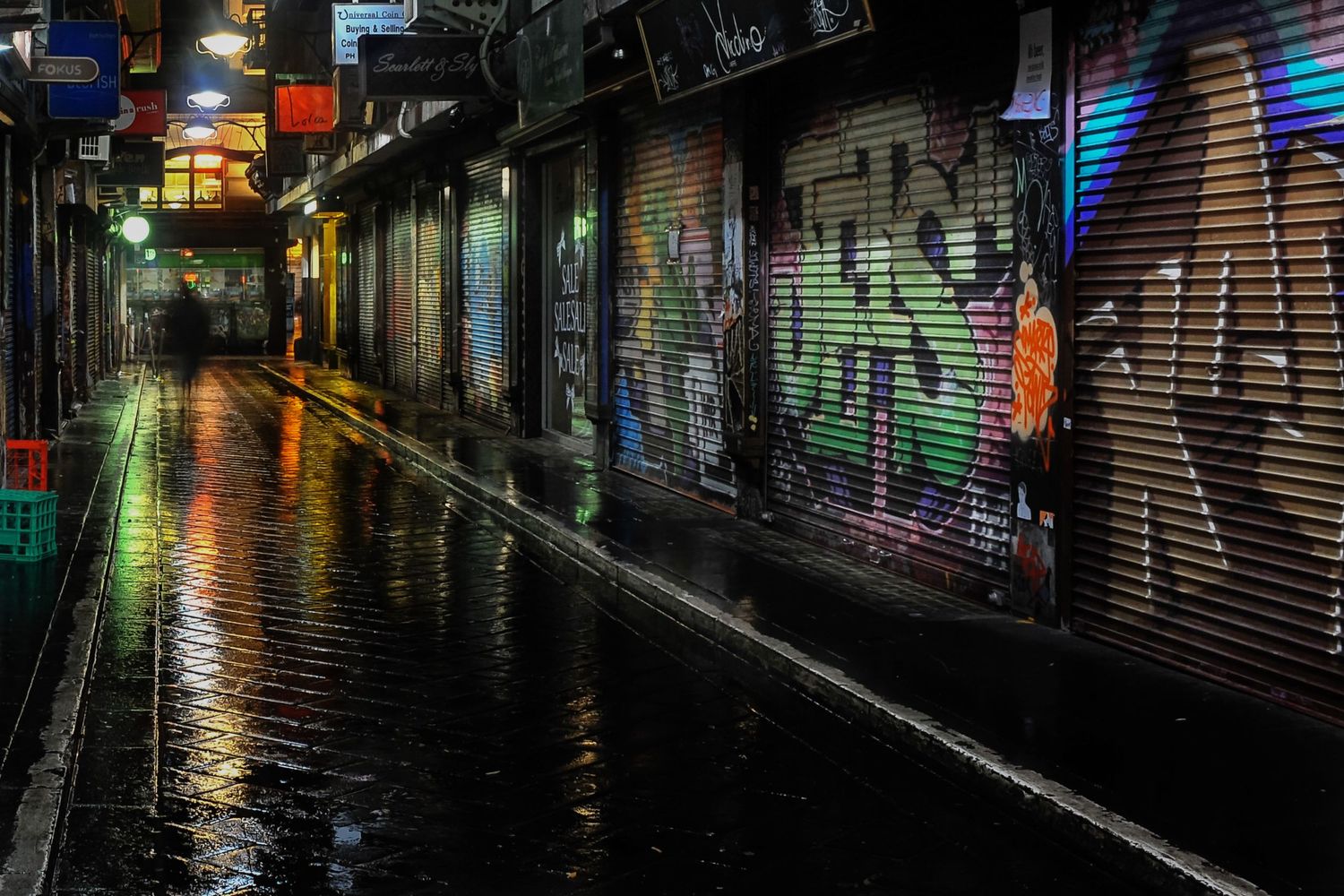 Rain-soaked graffiti-lined laneway reflecting city lights in Melbourne, Australia.
