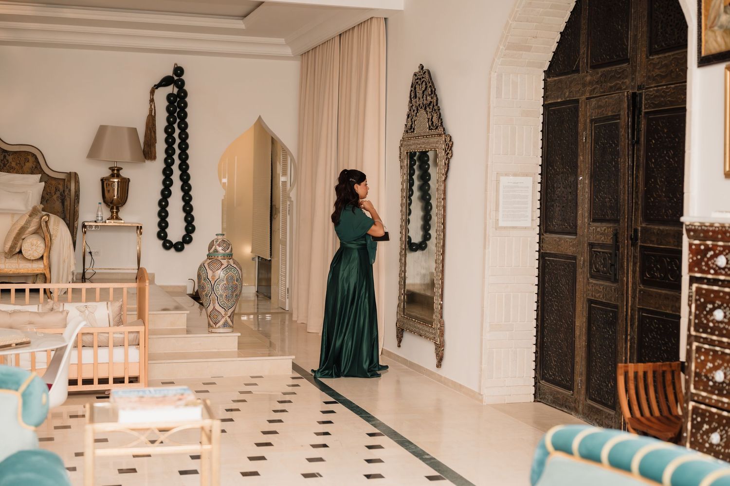 Woman in elegant green gown standing in a luxurious Moroccan-style interior.