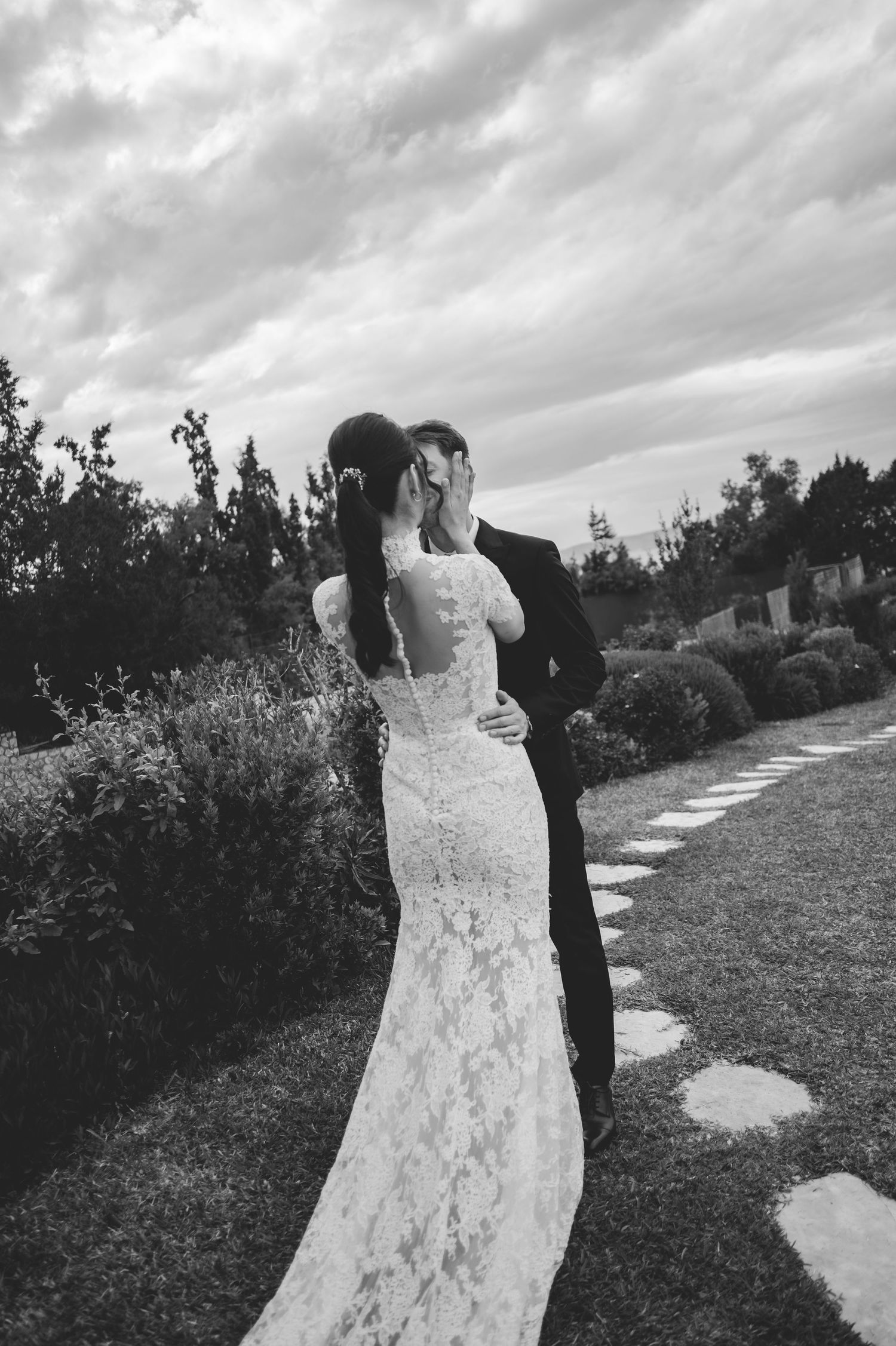 Black and white photo of bride and groom sharing a romantic kiss in a lush garden setting.