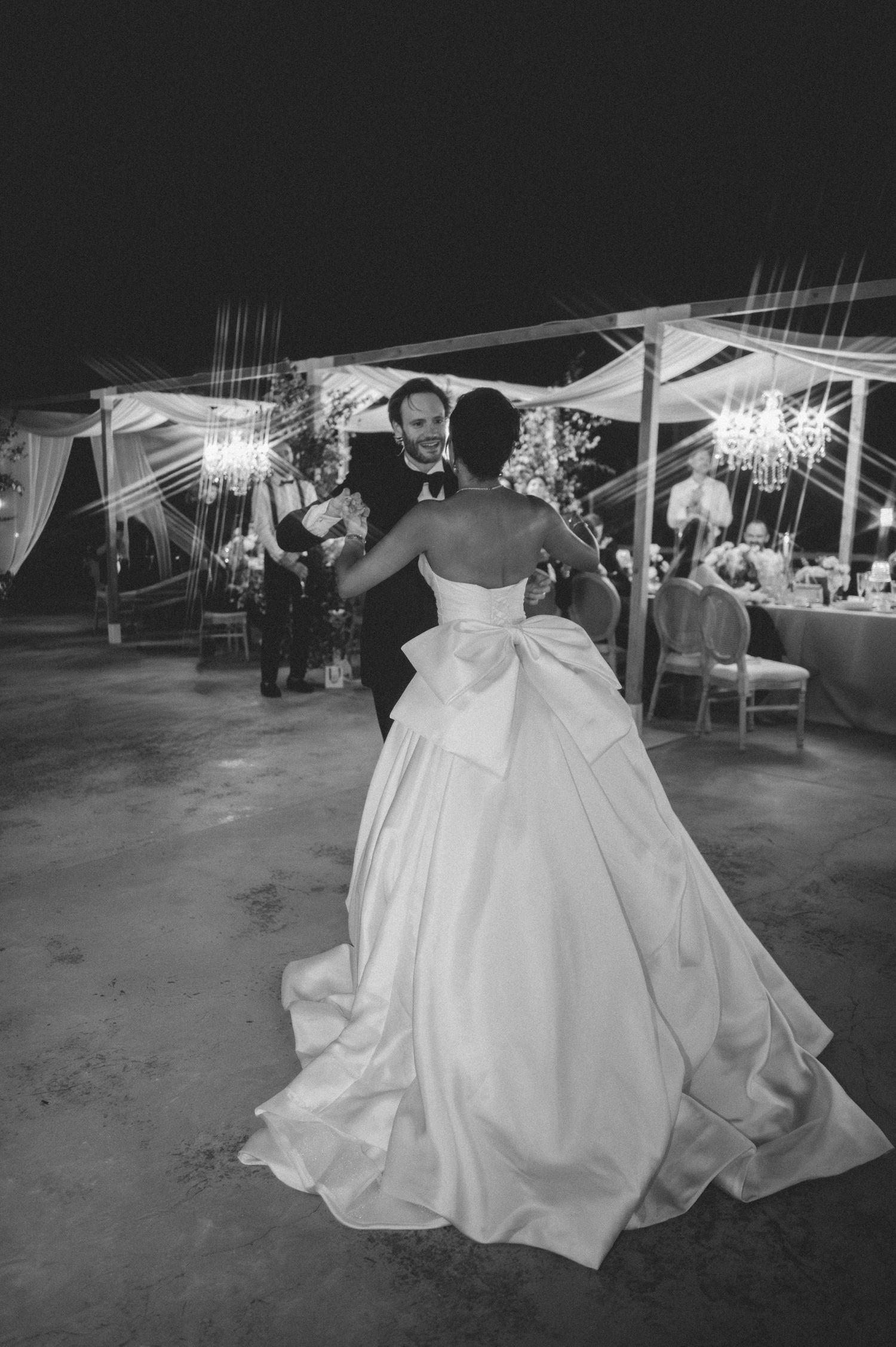 Bride and groom share first dance under sparkling chandeliers at elegant outdoor wedding reception at night.