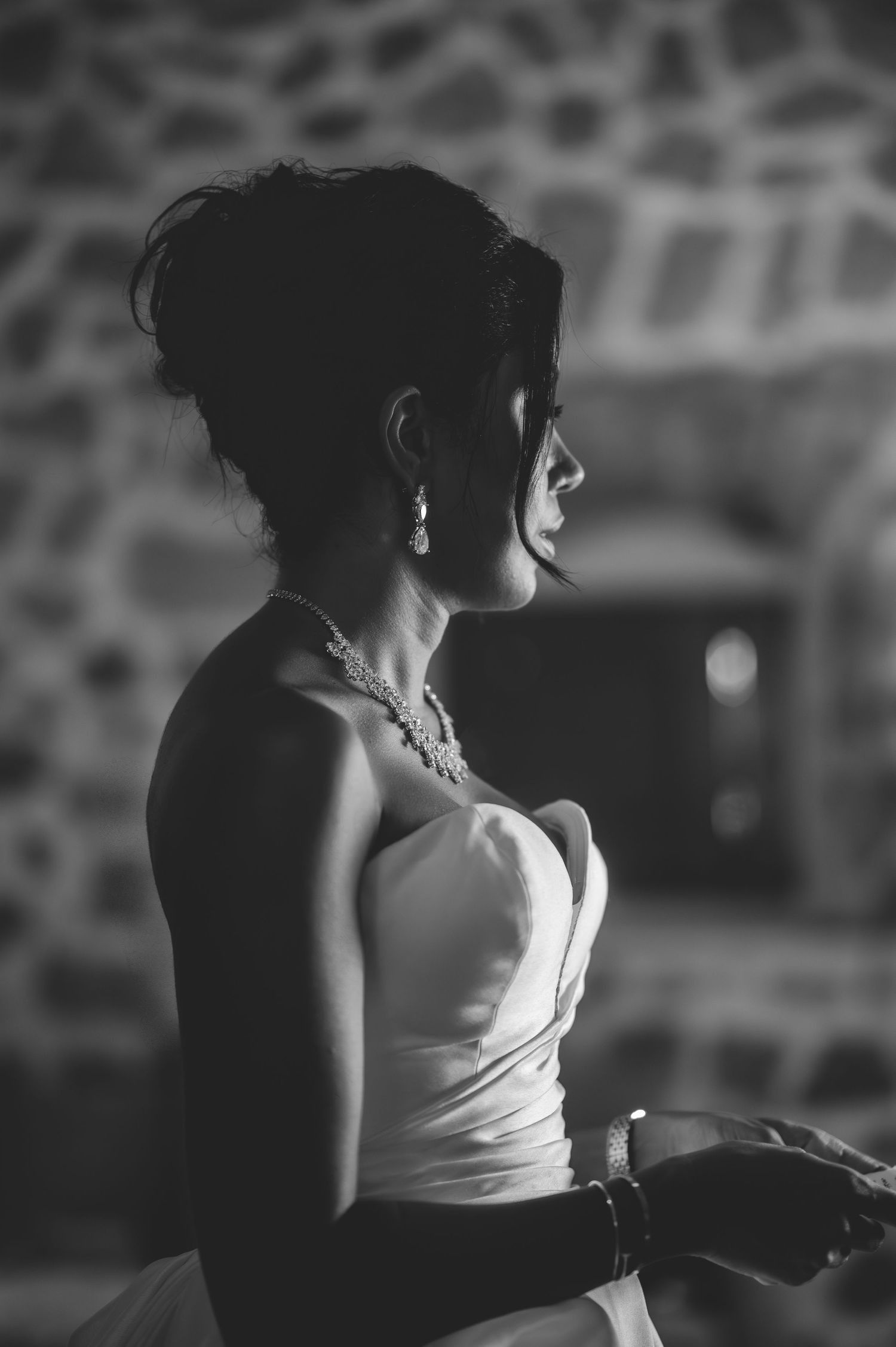 Elegant bride in strapless white gown with pearl necklace and earrings in dramatic black and white portrait.