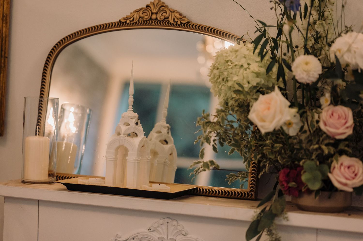 Elegant wedding decor with ornate gold mirror, white candles, and floral arrangement on mantelpiece.