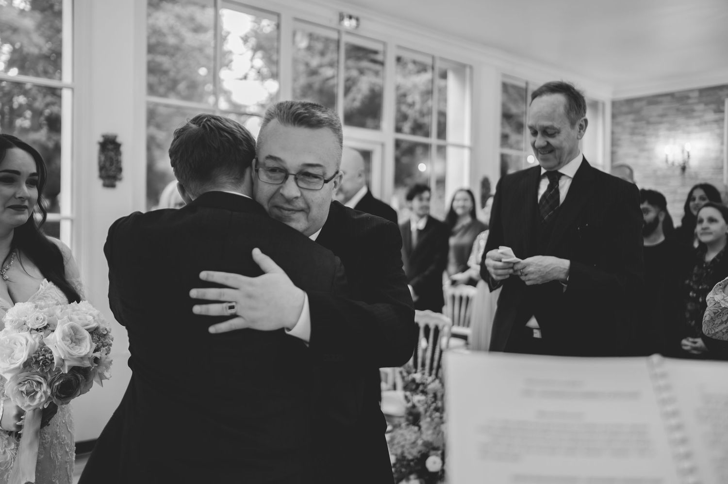 Emotional father hugs groom at wedding ceremony altar in classic black and white photography.