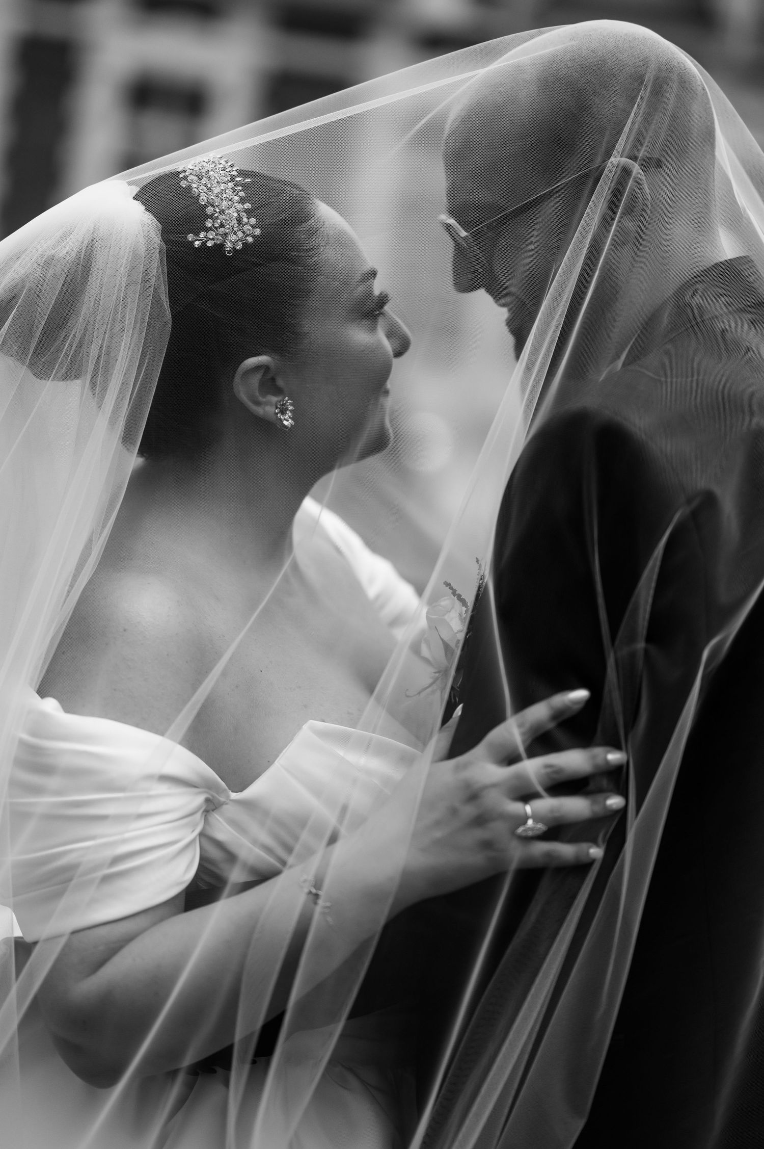 Black and white photo of bride and groom sharing intimate moment under wedding veil.