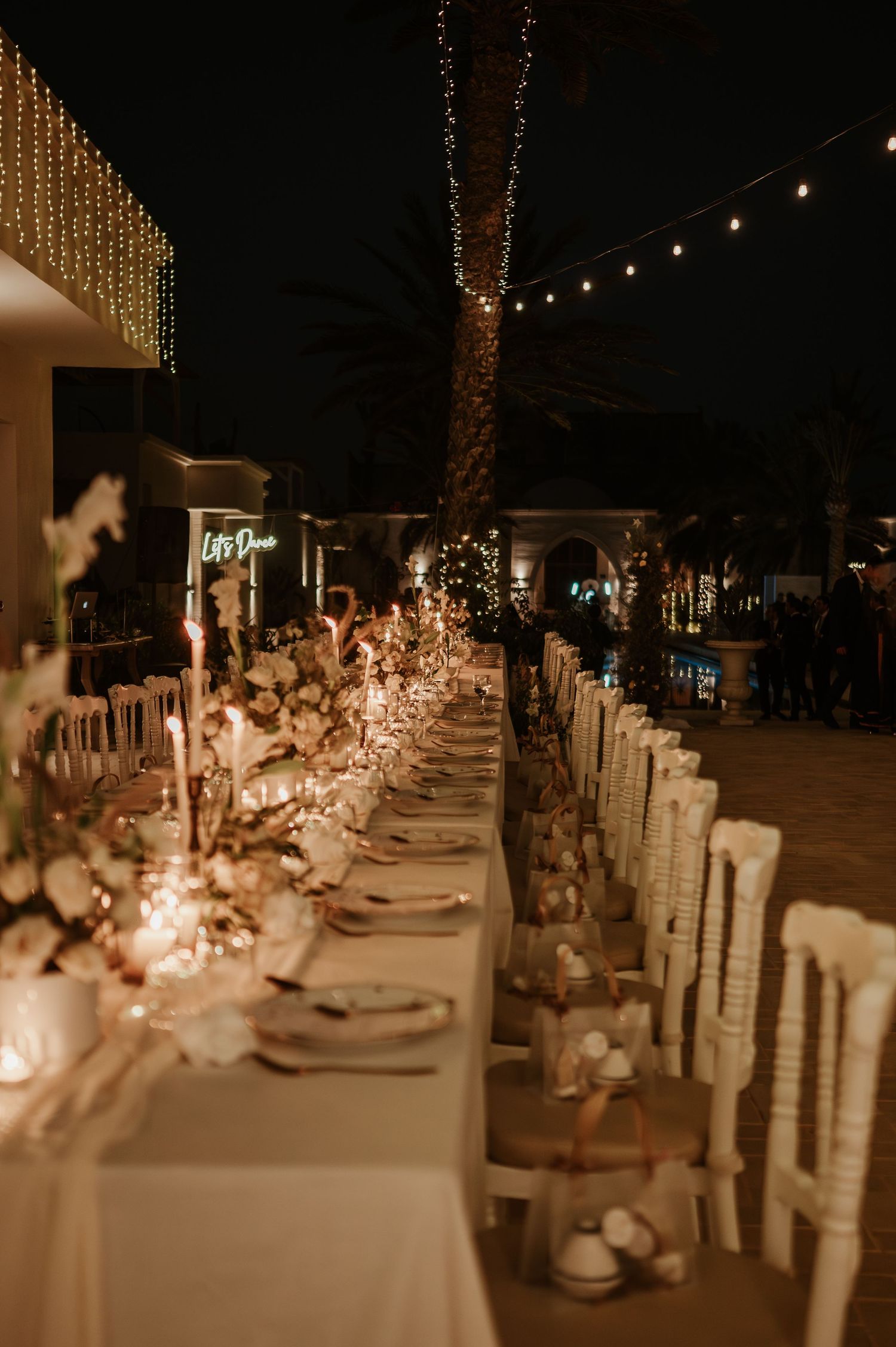 Stunning nighttime wedding reception with candlelit long table, string lights, and white floral centerpieces outdoors.